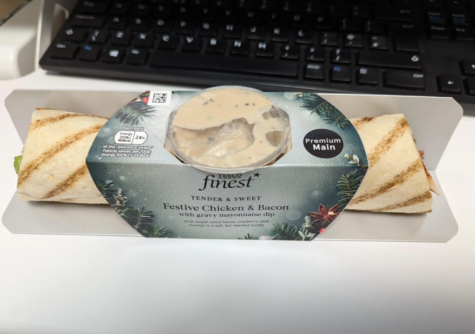 Packaged Tesco Finest Festive Chicken & Bacon wrap with gravy mayonnaise dip on a table, near a keyboard
