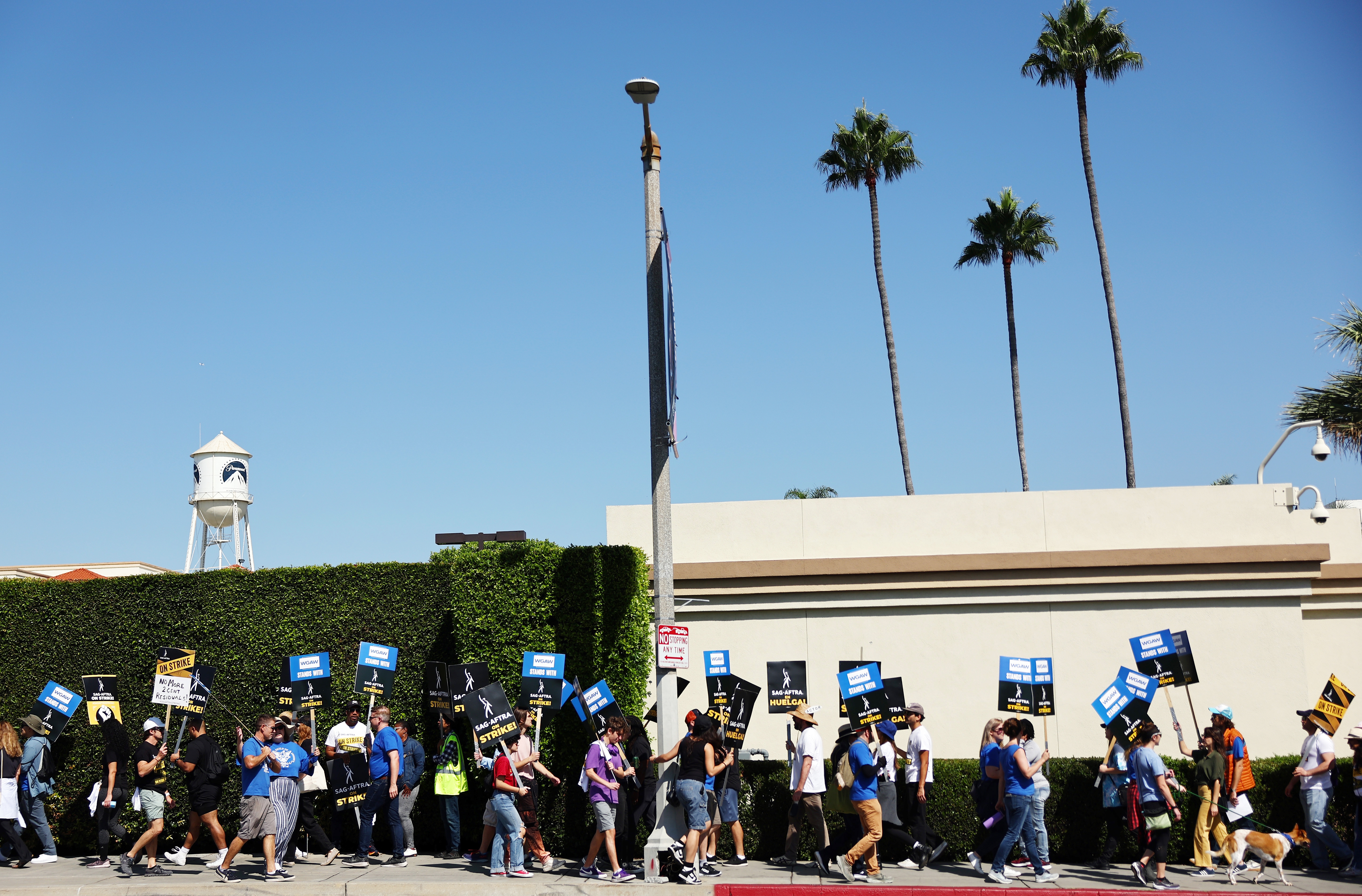 People marching in a protest holding signs, with palm trees and a water tower in the background