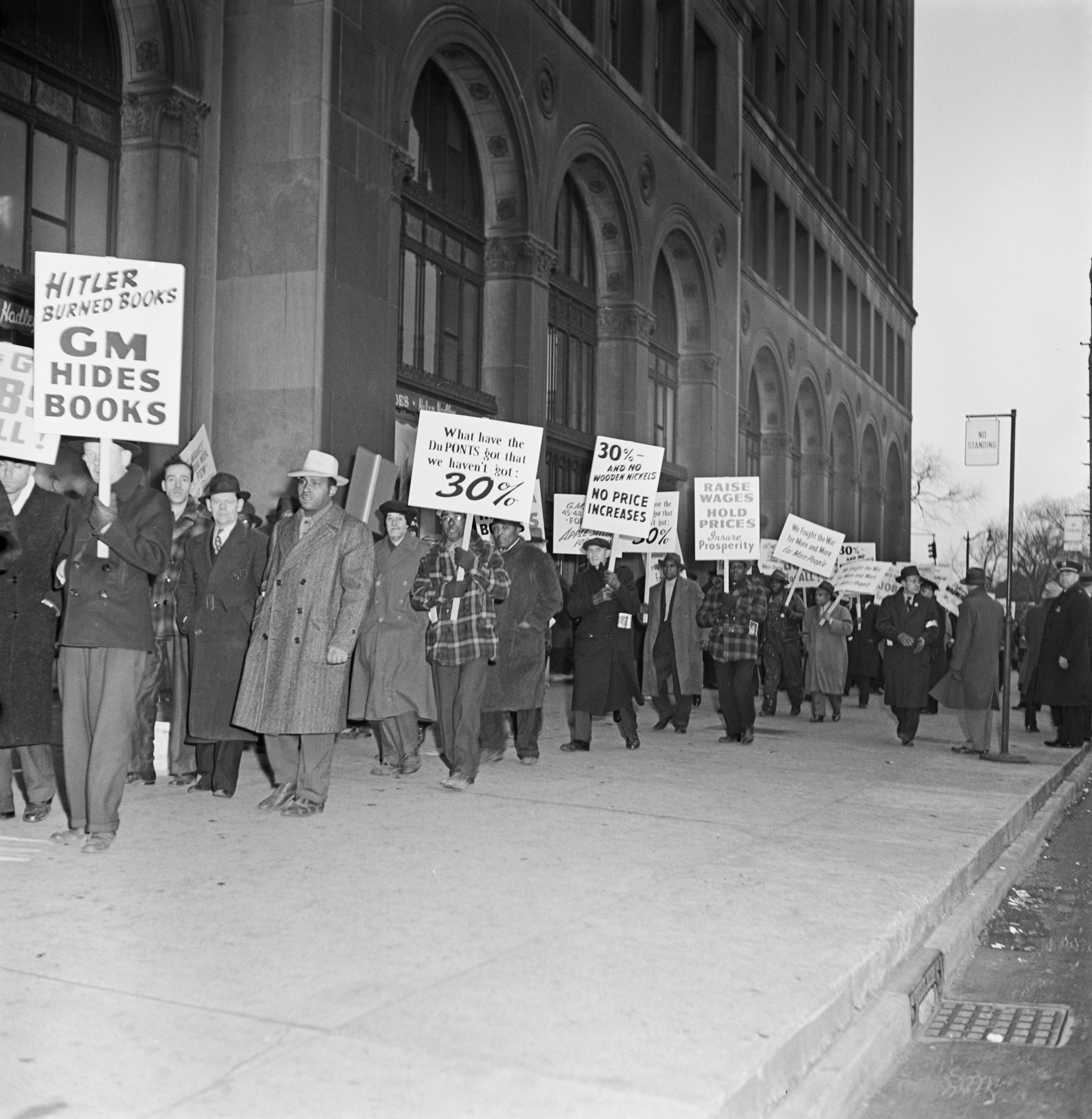 Protesters march with signs against GM outside a building, holding placards with messages about book hiding and free speech