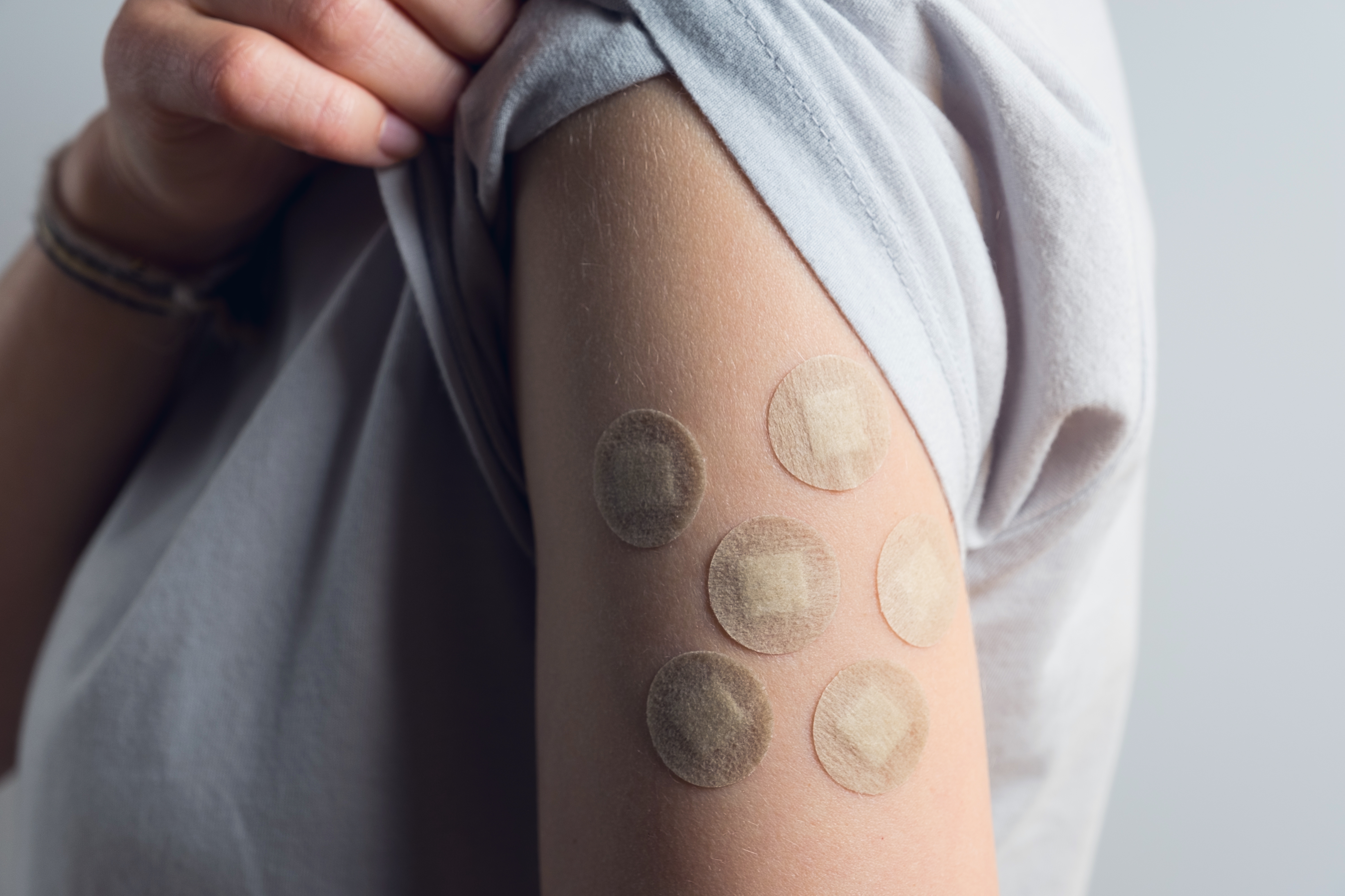 Arm with six small, round band-aids, suggesting multiple vaccinations, reflecting parental focus on child health and immunization