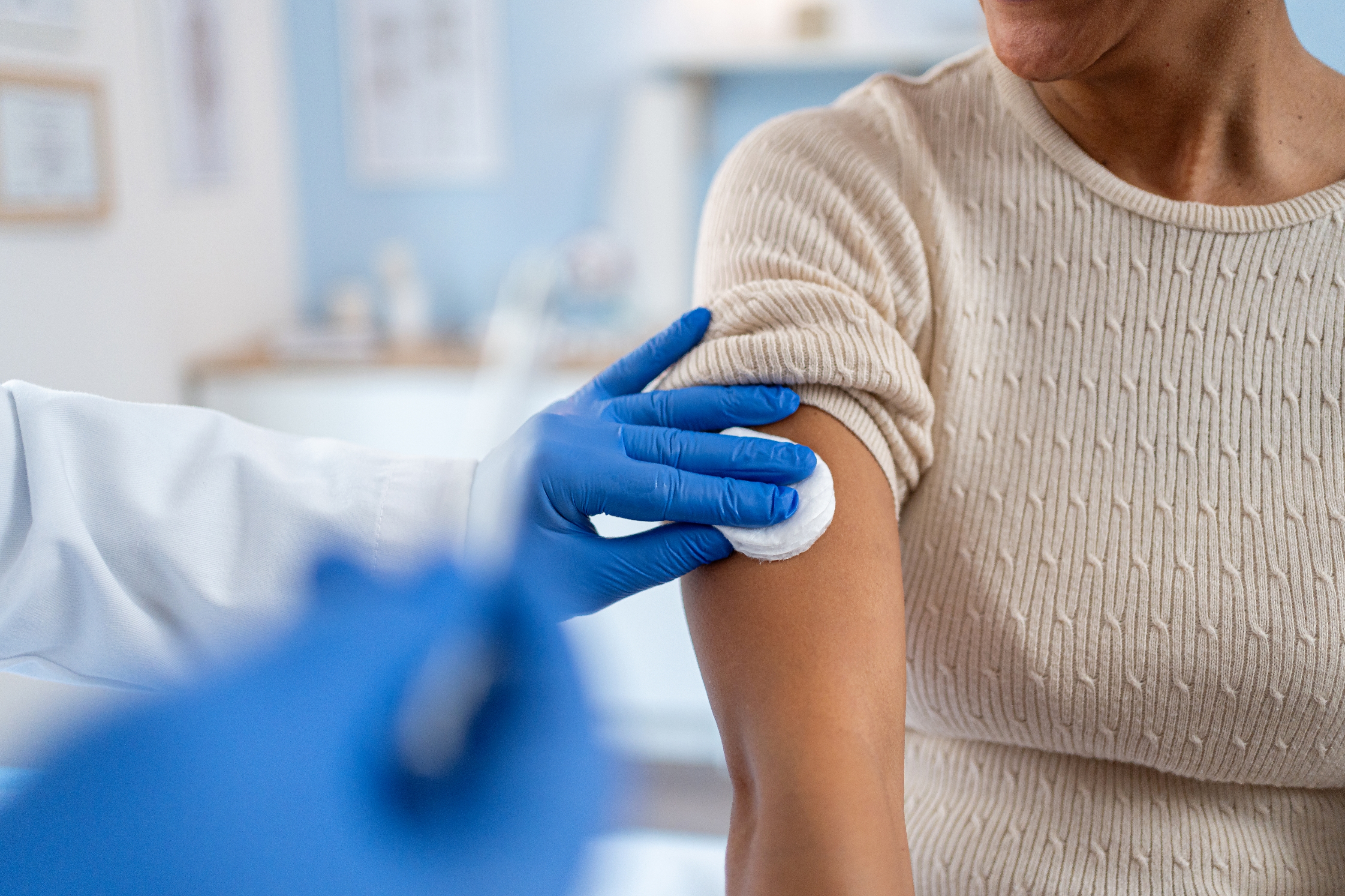 A doctor in white coat prepares to give a vaccination to a person, applying an alcohol swab to their upper arm