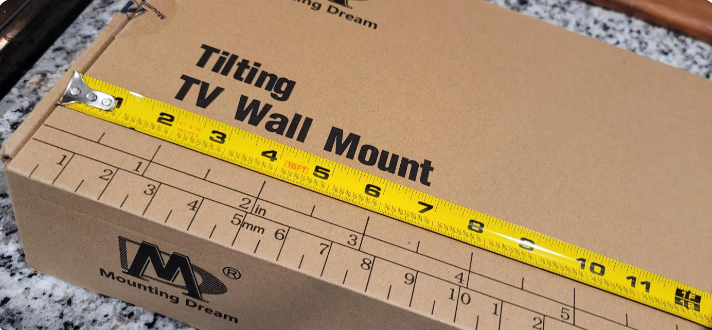Cardboard box labeled "Tilting TV Wall Mount" with a yellow tape measure on top