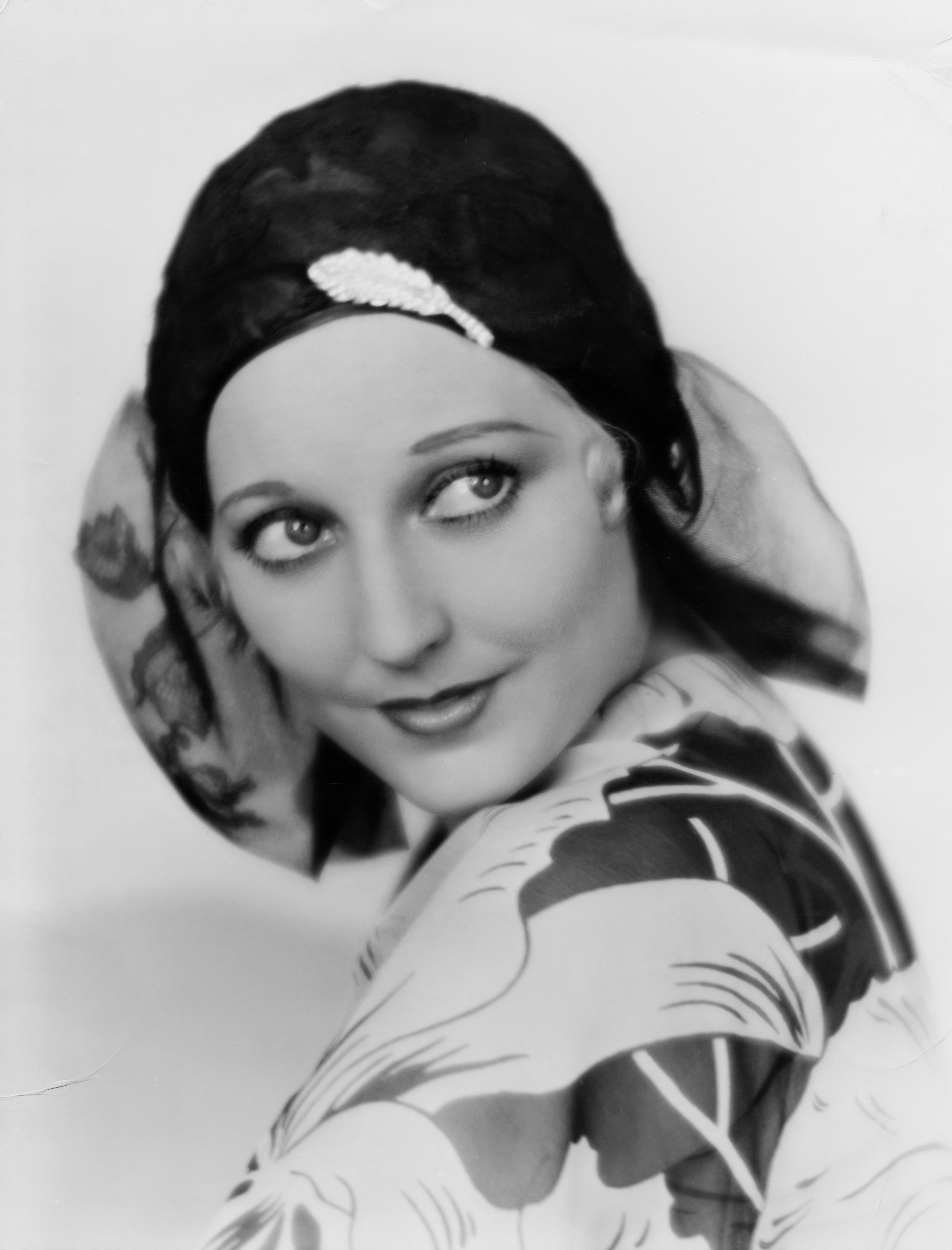 Person in retro headscarf and patterned top, looking over shoulder with an elegant, nostalgic expression
