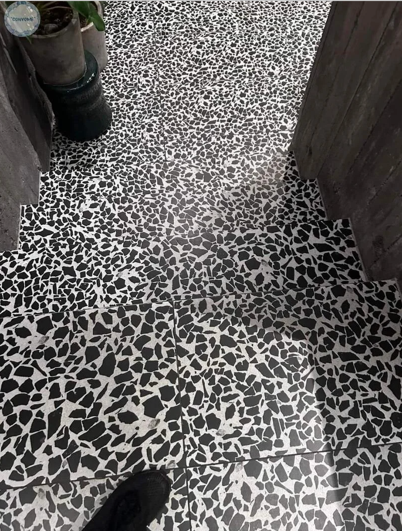 A floor with a black and white terrazzo-like pattern is partially seen from above, bordered by two potted plants