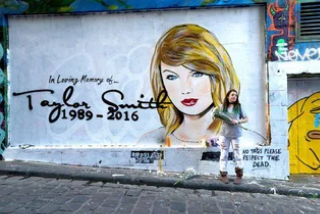 A person stands holding flowers in front of a mural depicting a tribute to "Taylor Smith, 1989-2016," with a note to "Please respect the dead"