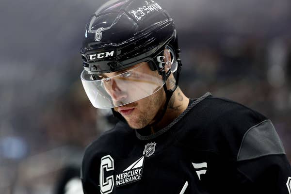 Hockey player wearing a black uniform and helmet on the ice, focused. Jersey features a captain&#x27;s &quot;C&quot; and sponsorship logos