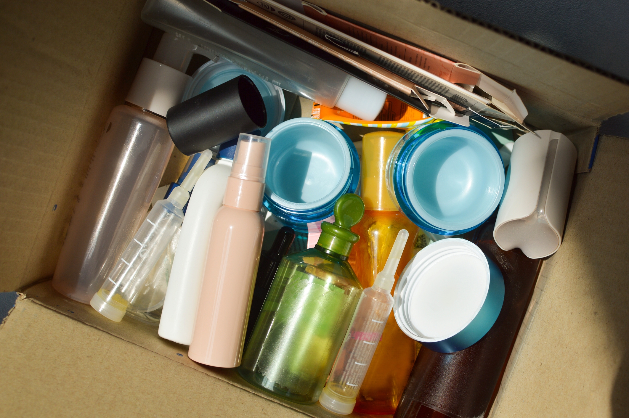 Open cardboard box filled with assorted empty plastic containers, including bottles and jars, viewed from above