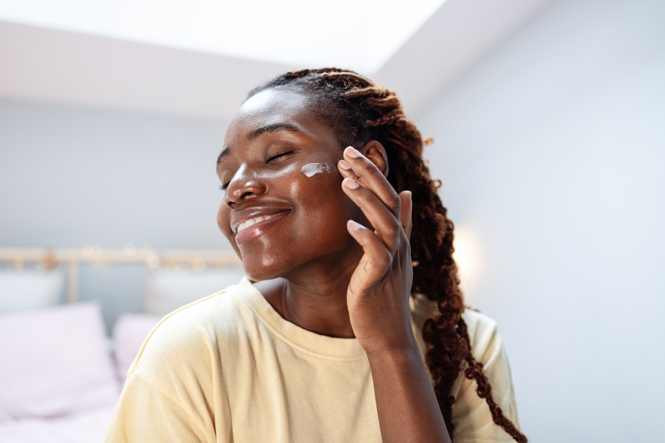 Person smiling and applying facial cream, enjoying a skincare routine in a cozy room