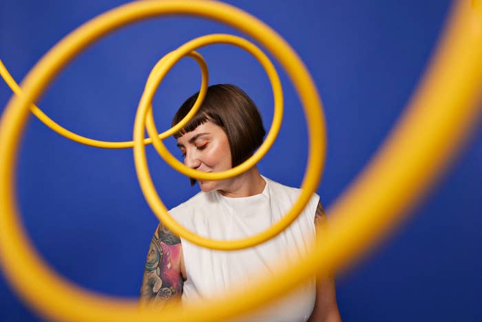 Person with tattoos and short hair stands behind artistic, coiled objects, creating a dynamic visual effect