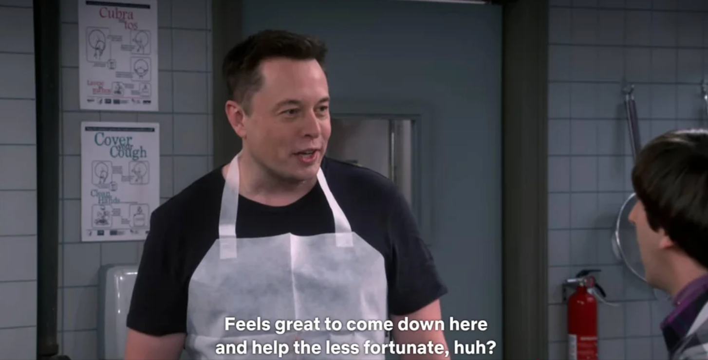 Musk standing in a kitchen wearing an apron, talking to someone off-camera. Subtitles read: "Feels great to come down here and help the less fortunate, huh?"