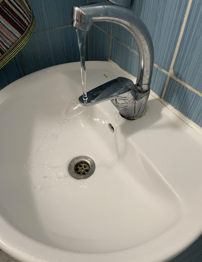 Water flows from a faucet into a slightly clogged bathroom sink, with some water pooling around the drain