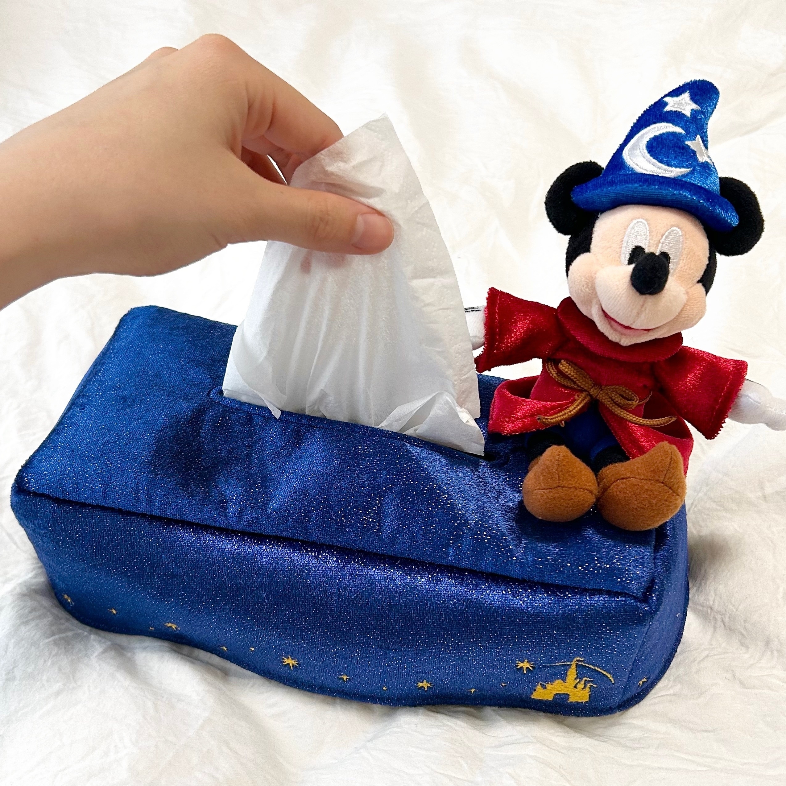 ぬいぐるみ付きのティッシュボックスを持ち上げる手。魔法使いの衣装を着たキャラクターが座っています。