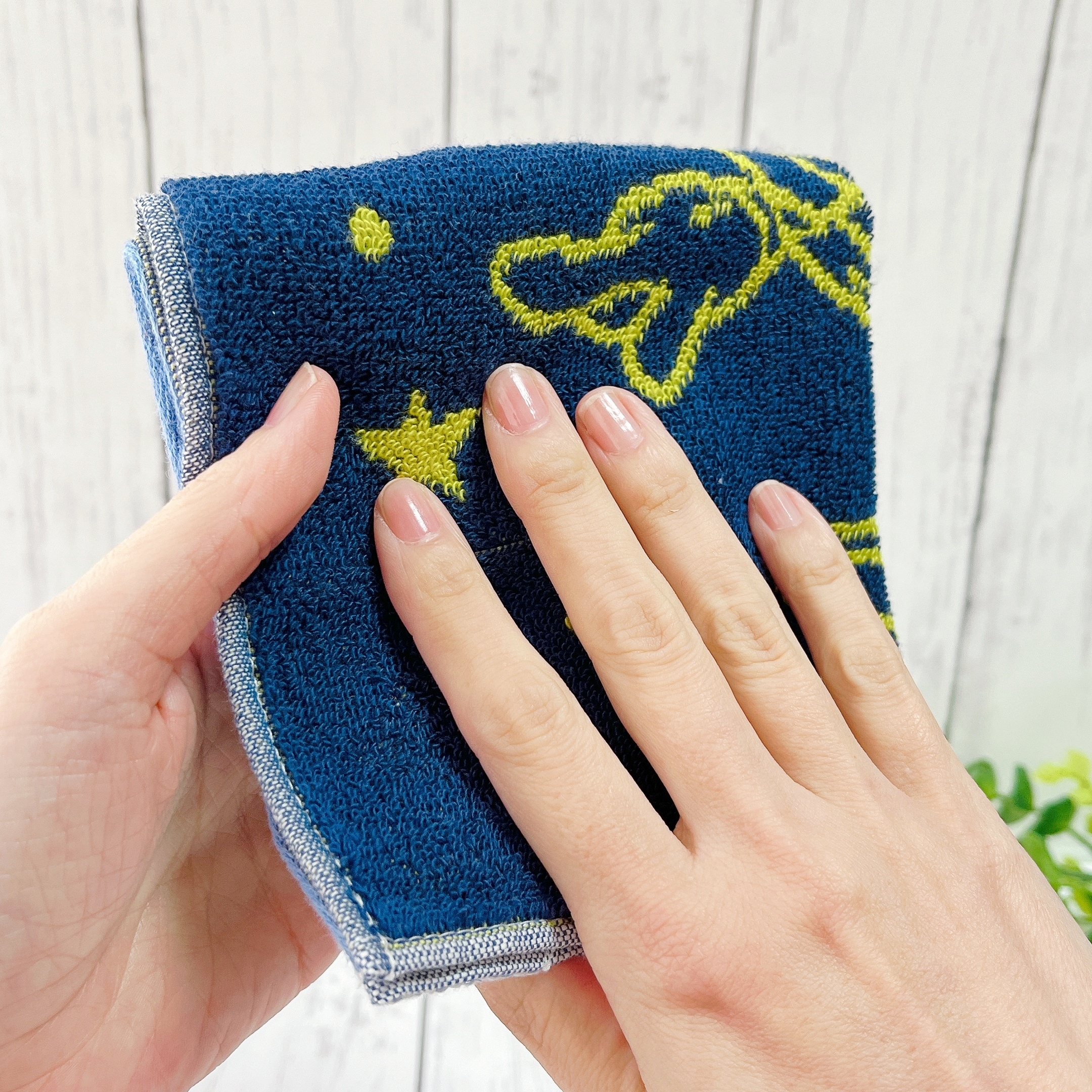 手のひらに青いタオルを持ち、柔らかさを感じています。タオルには黄色い星と恐竜のデザインがあります。