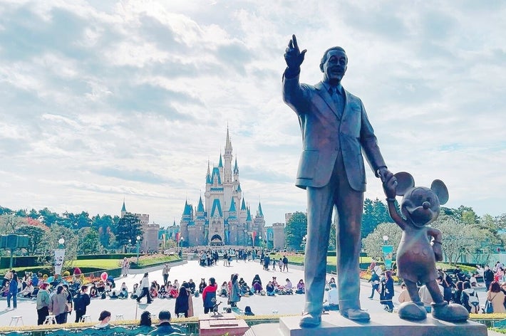 ディズニーパークにあるウォルト・ディズニーとミッキーマウスの像。背後にシンデレラ城が見える。多くの来場者が周囲にいる。