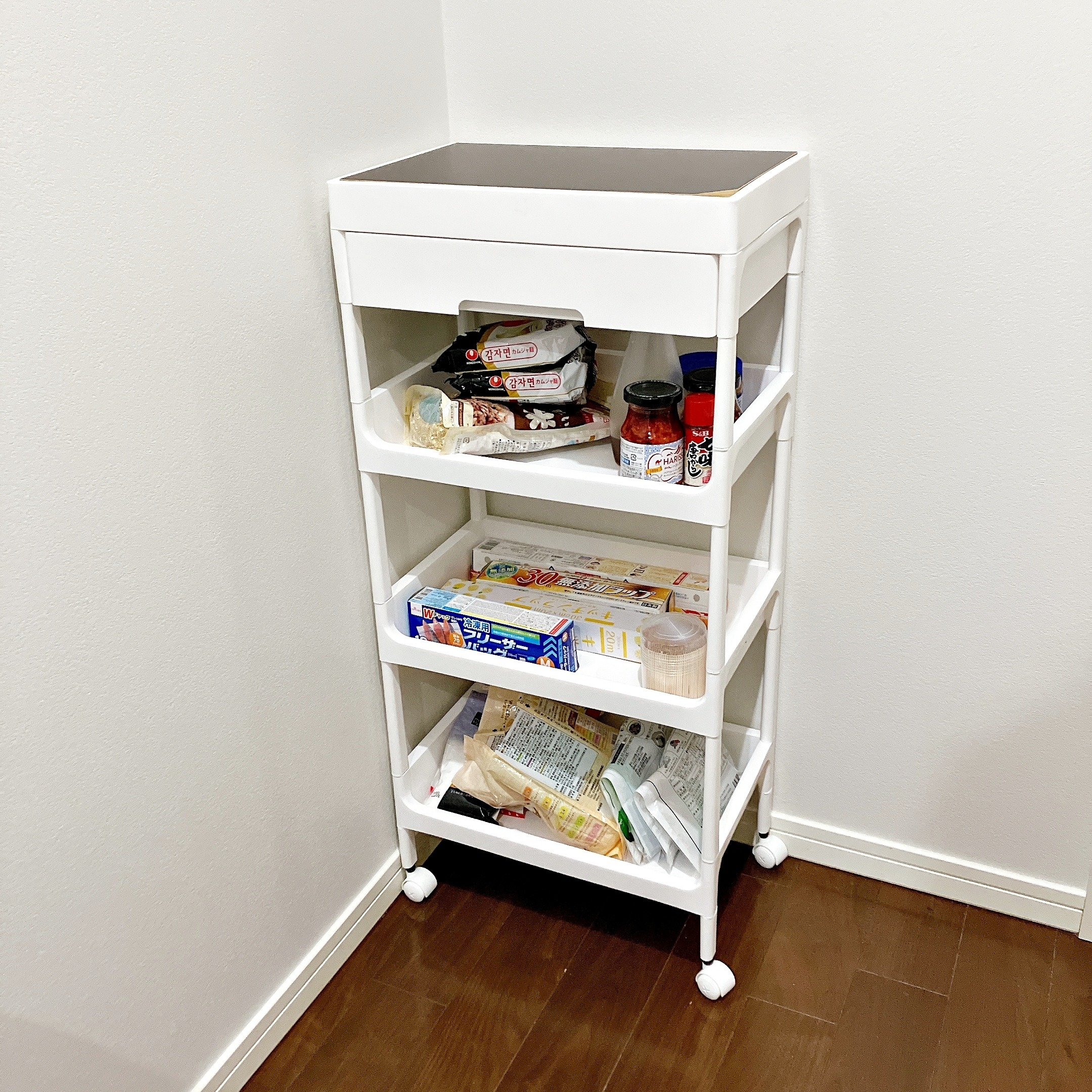 キッチンの隅に置かれた食品収納ワゴン。棚にはジャム、スナック、缶詰などの食品が整然と並んでいる。