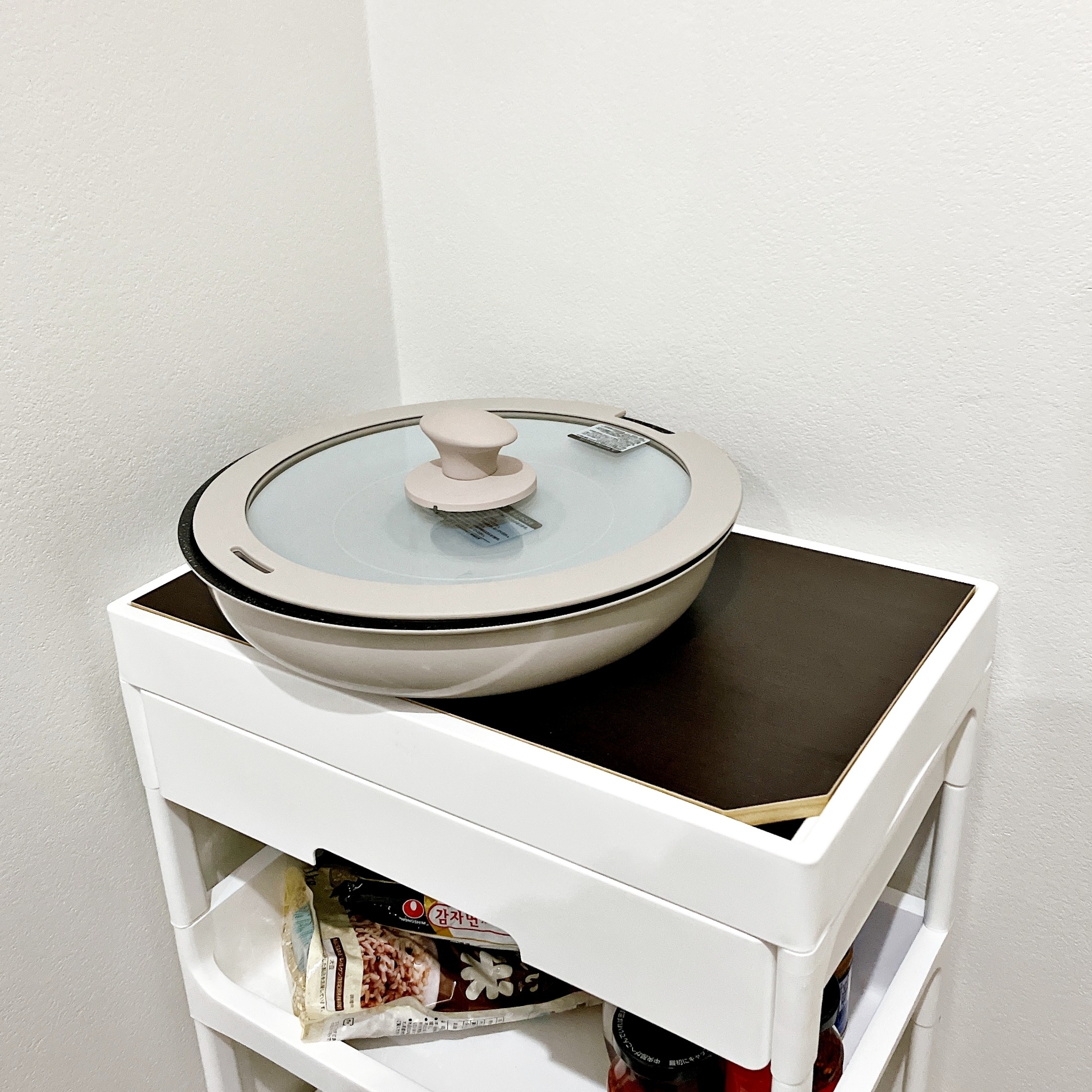 鍋の蓋付きの調理器具が白い収納棚に置かれている。棚の下段には料理本や瓶が収納されている。