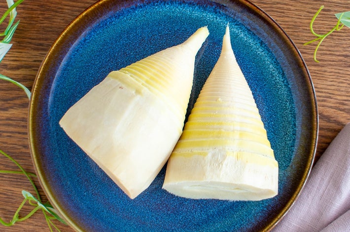 お皿に盛られた二つの筍がテーブルに置かれている。周囲に植物が見える。