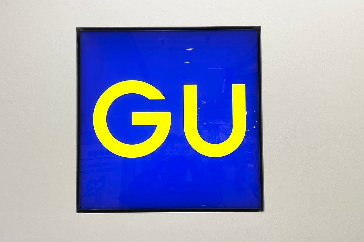 A sign with large yellow letters "GU" on a blue background, likely indicating a store logo