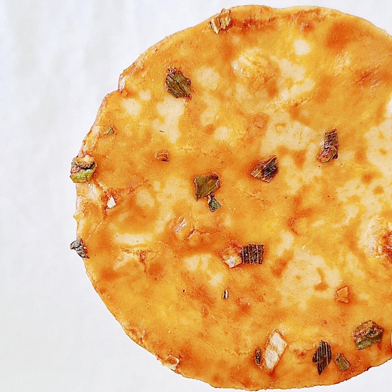 せんべいのクローズアップ。焼き色がついており、刻んだネギが散らばっている。