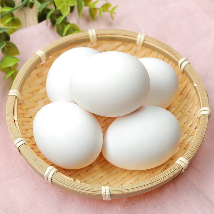 ざるに入った5つの卵。背景に緑の葉が見える。