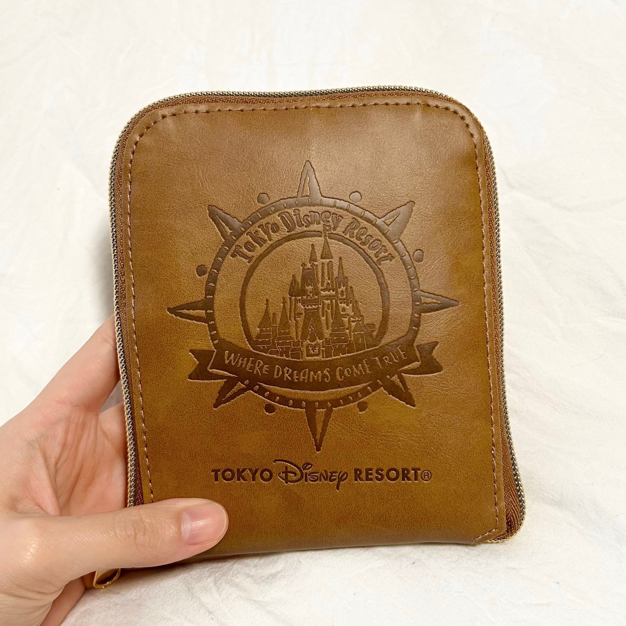 手に持たれた、東京ディズニーリゾートのロゴが刻まれた革製のポーチ。