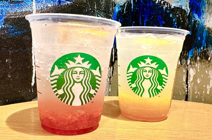 テーブルに置かれた2つの透明なスターバックスカップ、果物入りの冷たいドリンクが入っている。背景は抽象的な壁画。