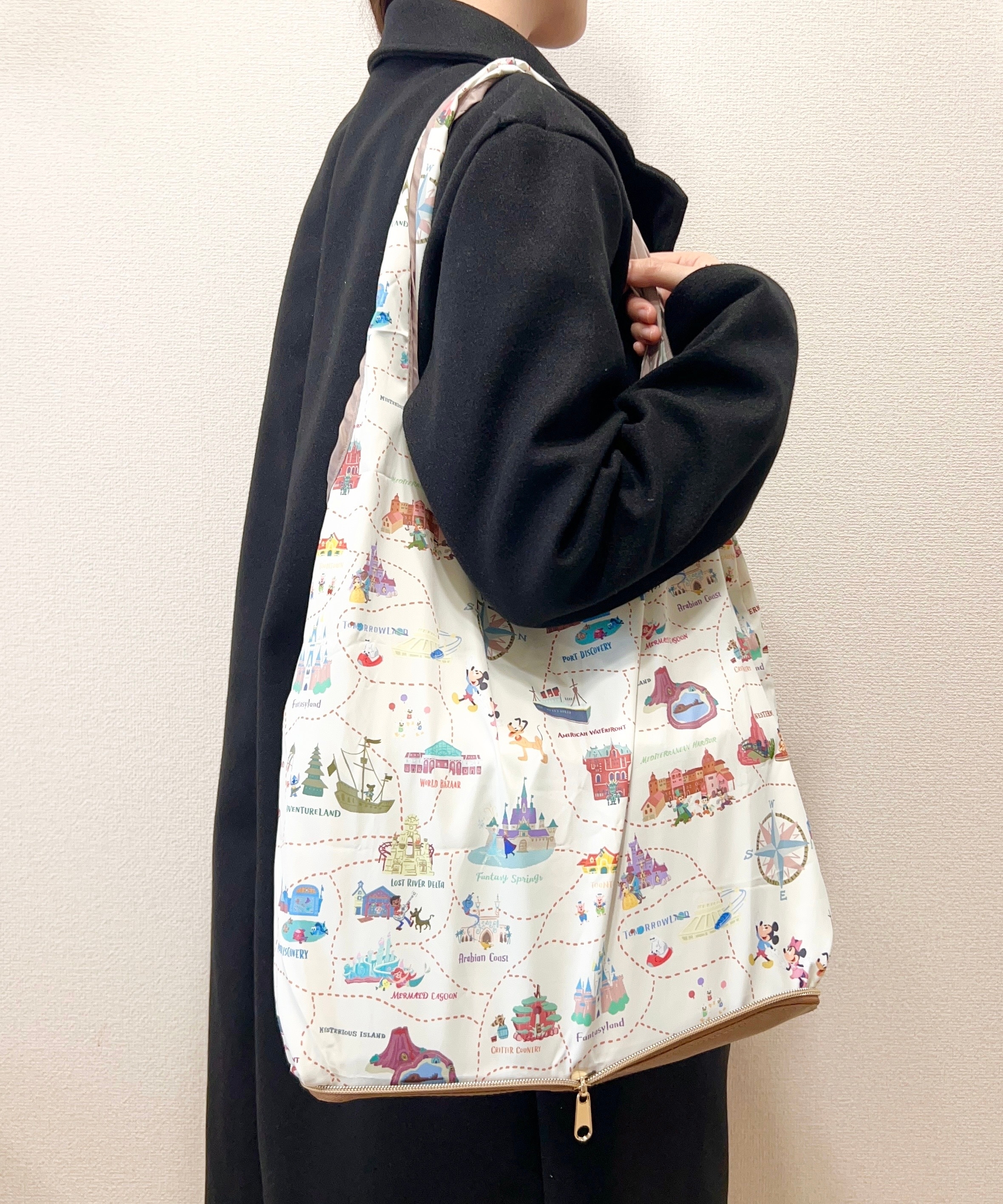 白い地図柄の大きなバッグを肩にかけた人が、黒のコートを着て横向きに立っている。