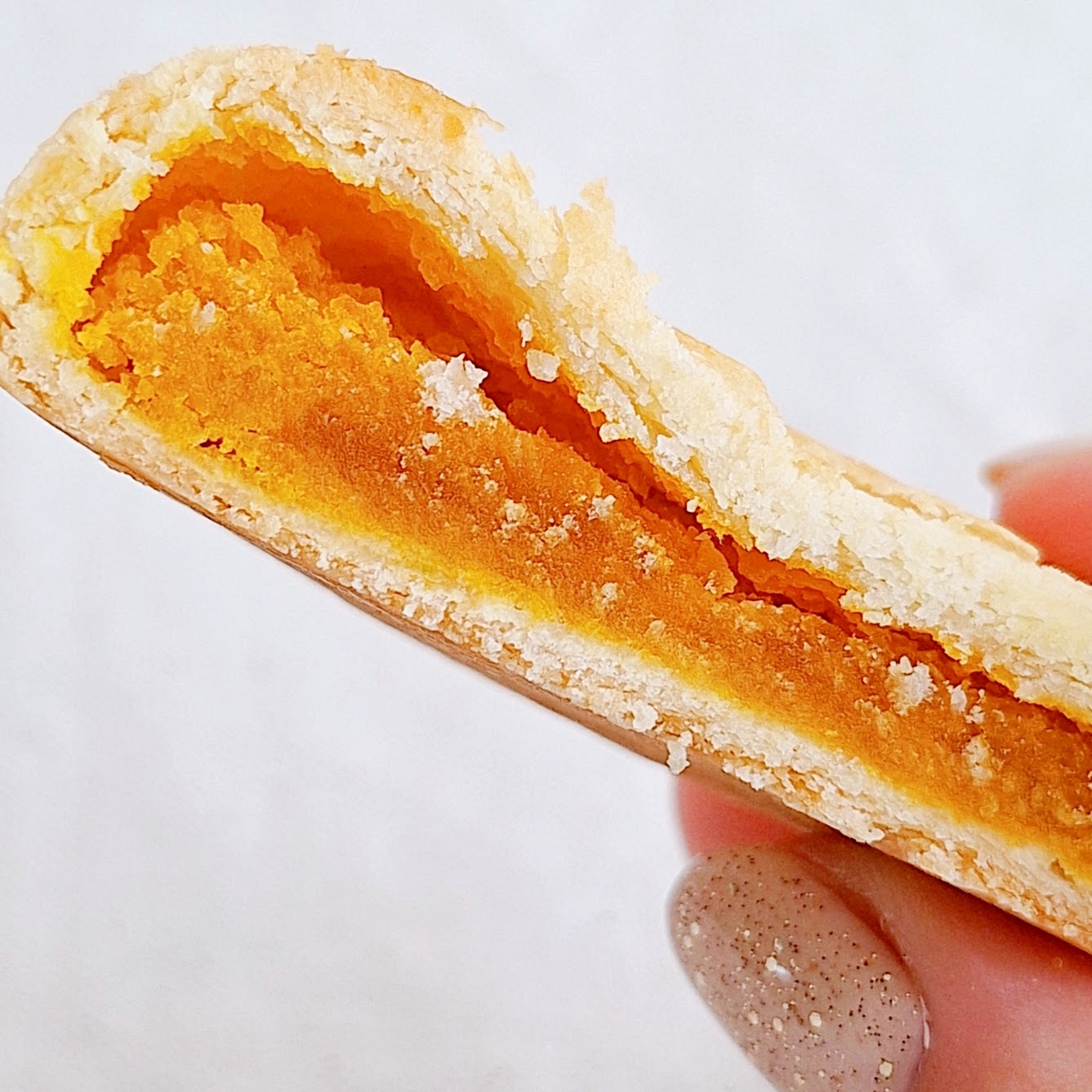 クッキーの断面。柔らかいオレンジ色のフィリングが詰まっている。指で持たれている。