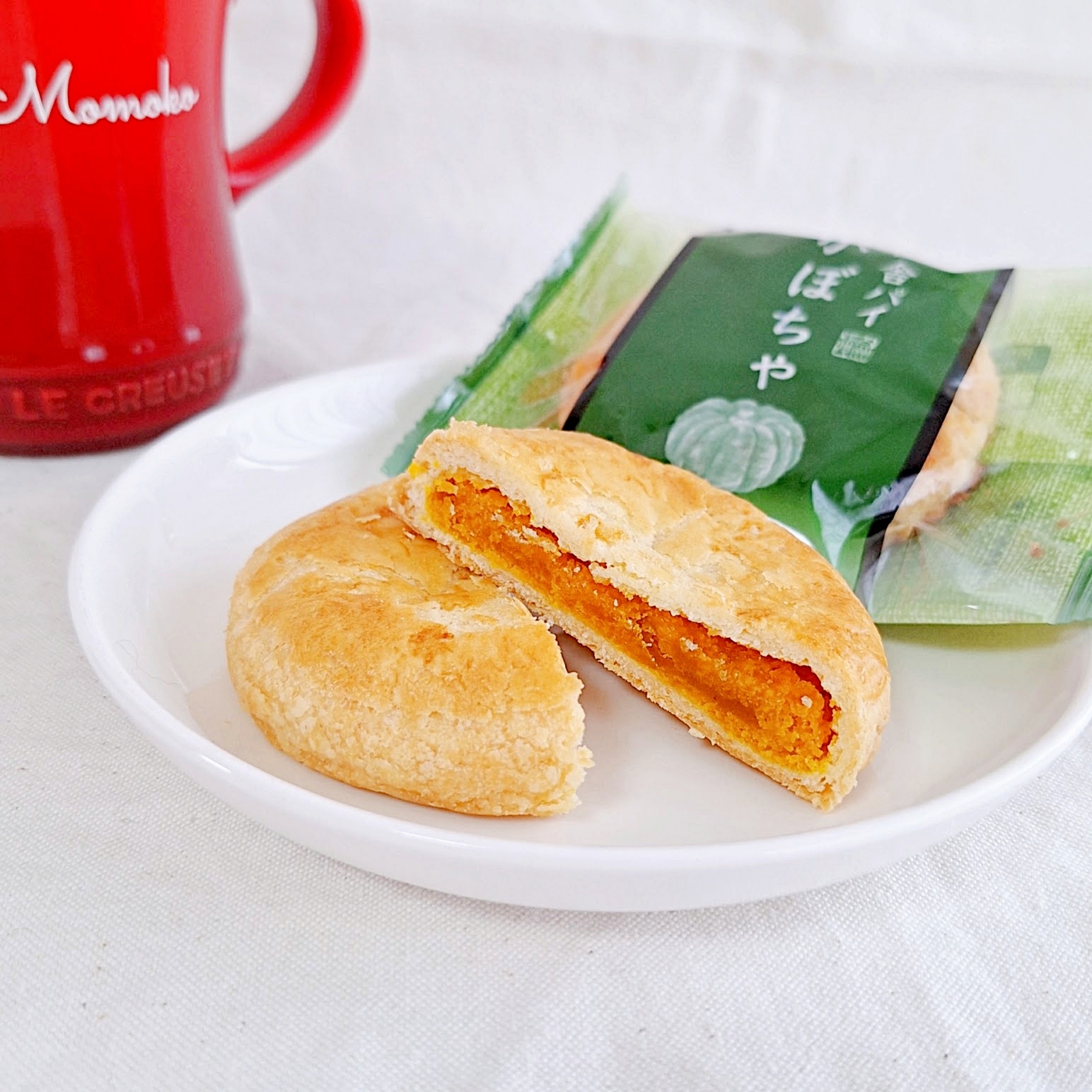 割れたパンプキンパイが皿に乗っている。背景に未開封のパイと赤いマグカップが見える。