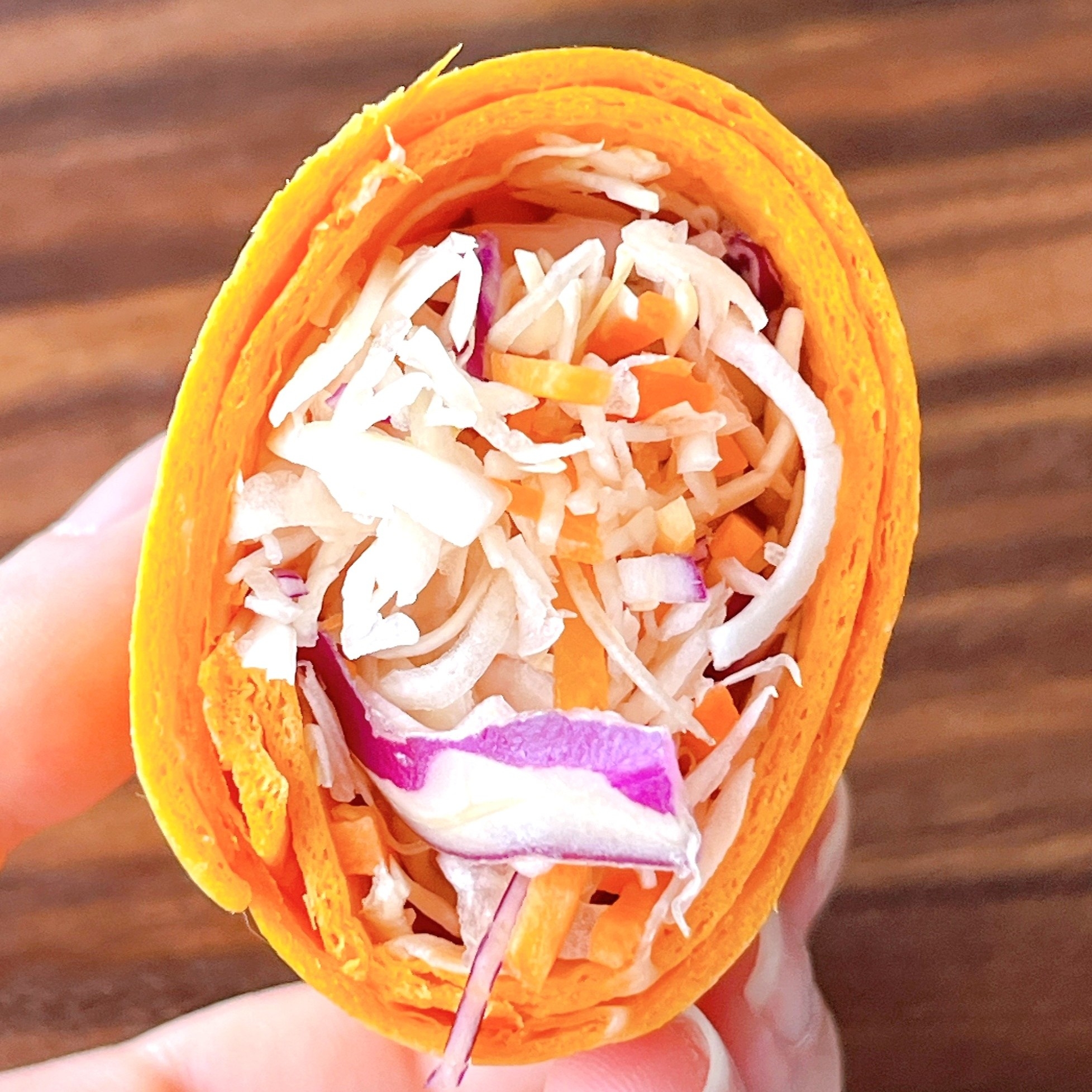 野菜の千切りを詰めたラップサンドイッチが手に持たれている様子。