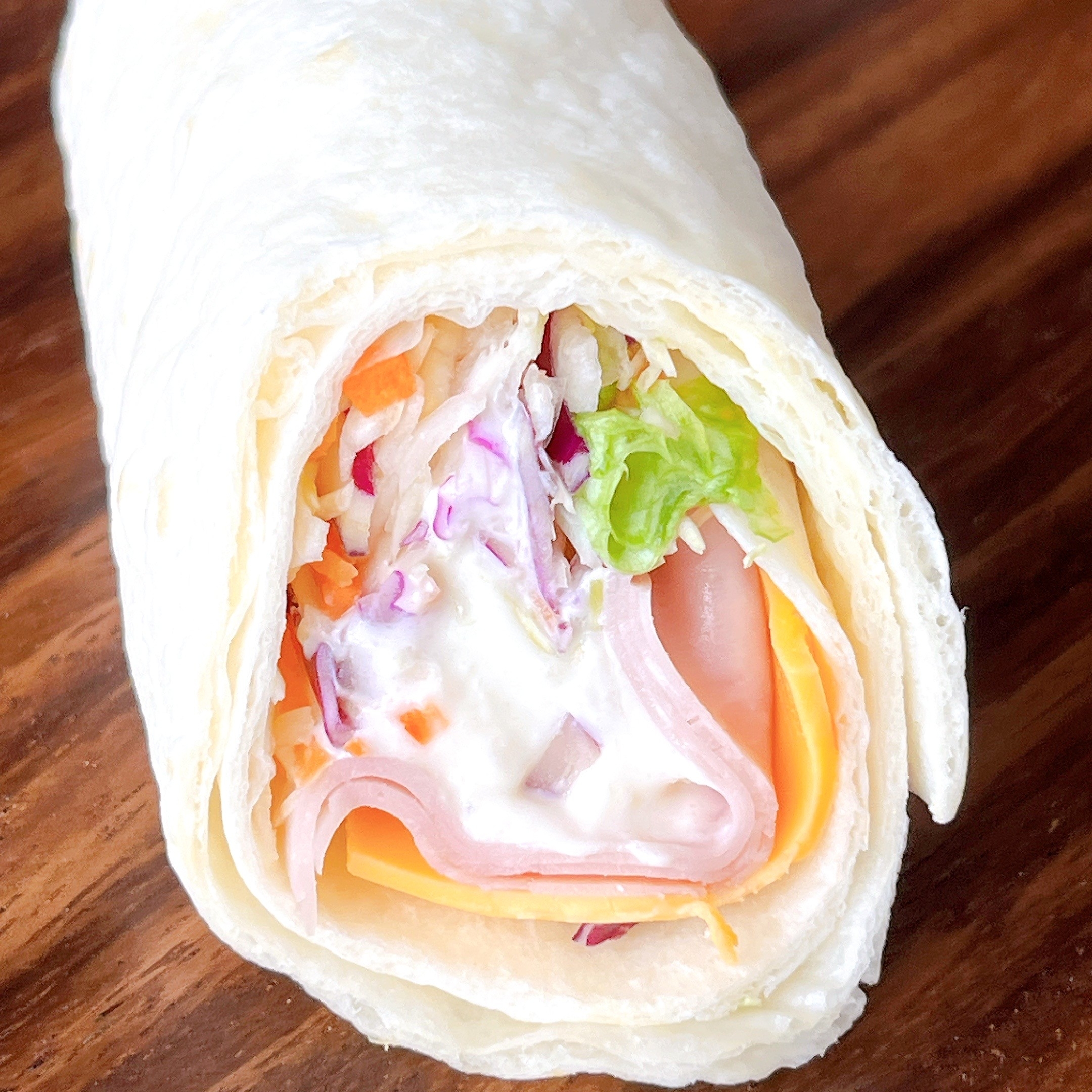 トルティーヤに包まれたハムとチーズのラップサンドイッチ。野菜とドレッシングが入っています。