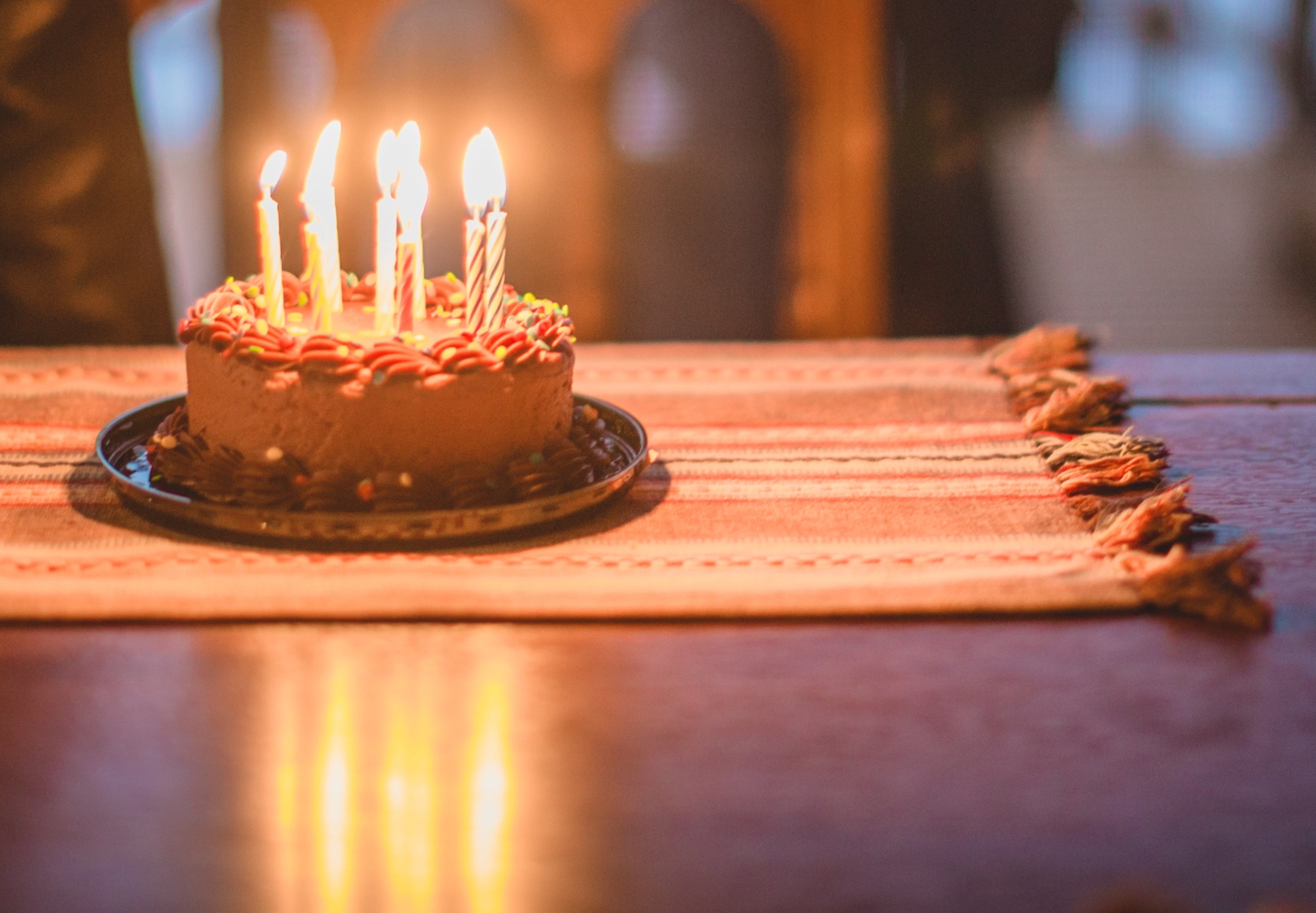 Child in leather jacket looks at a cake with lit candles, set on a dining table