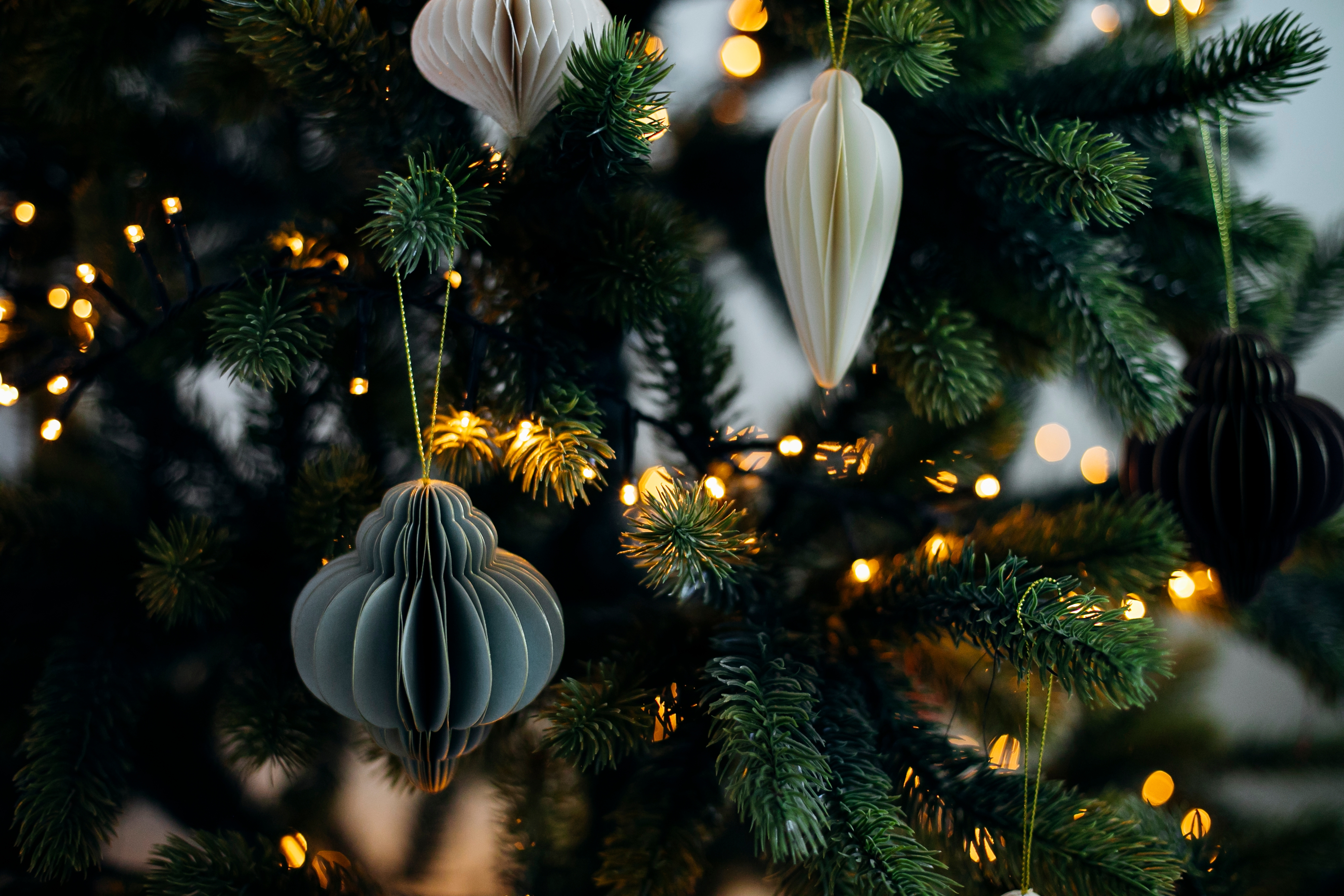 Decorative paper ornaments hanging on a Christmas tree with warm, glowing lights
