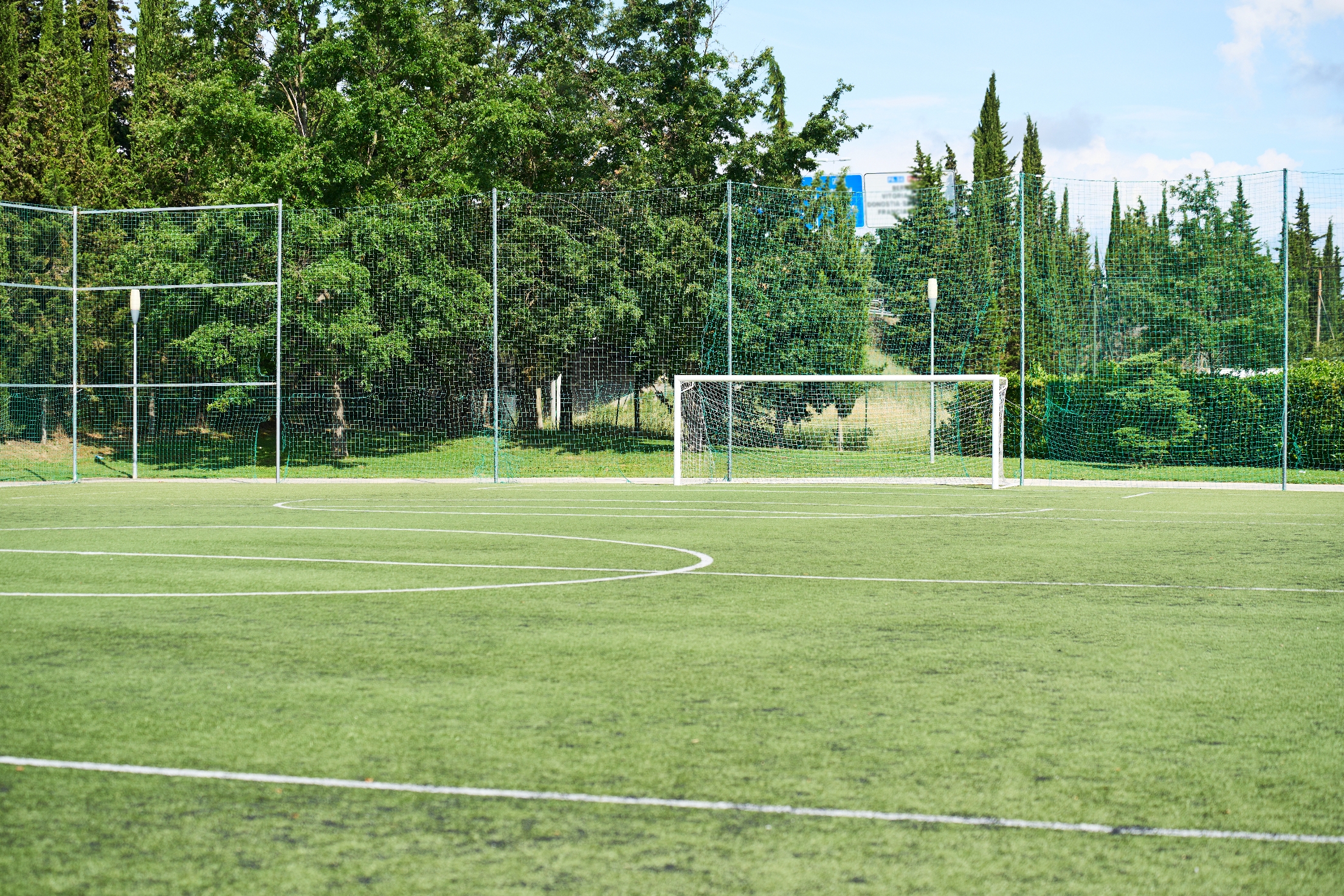 An empty soccer field with green grass and a goalpost, surrounded by trees and fencing