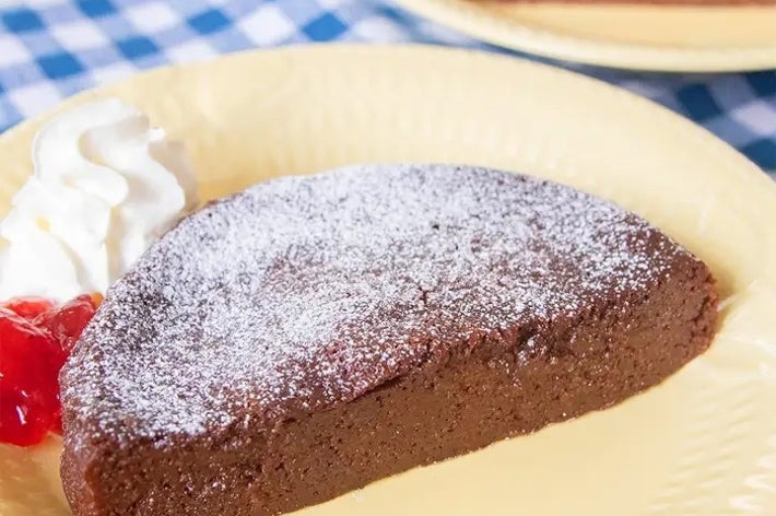 皿に盛られたチョコレートケーキの一切れ。上に粉砂糖、横にホイップクリームとチェリー添え。