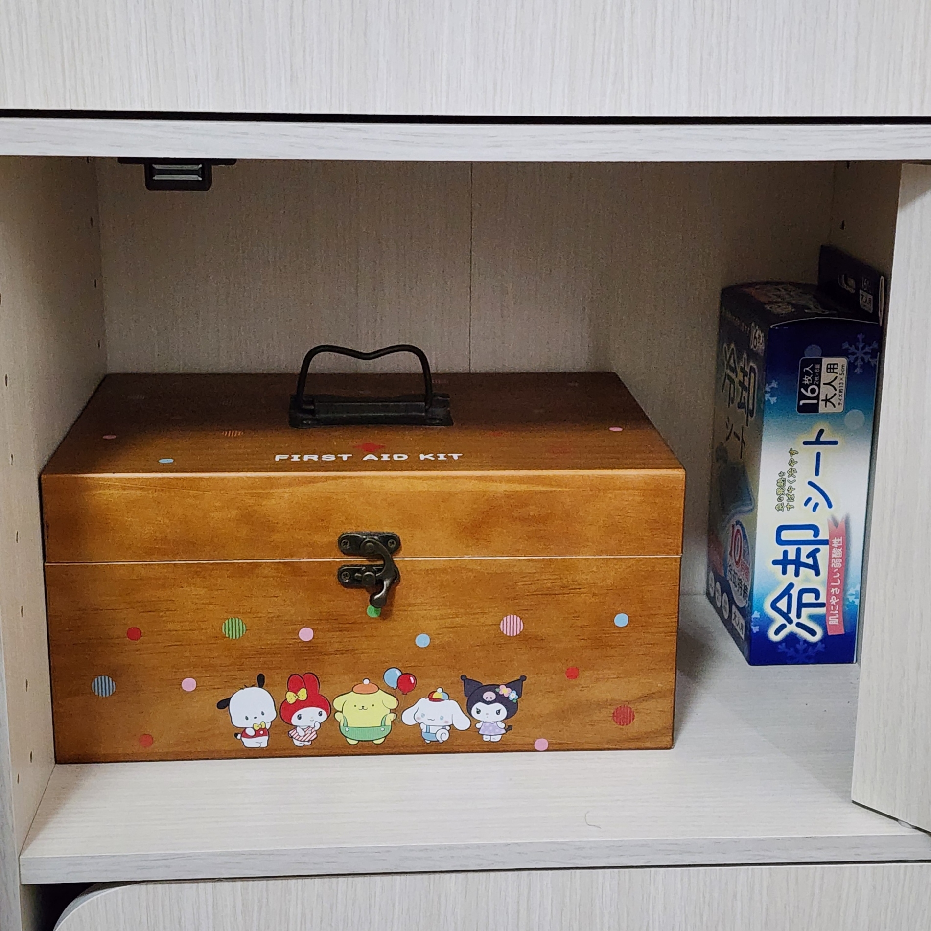 棚に収納された木製の救急箱と、横に置かれた冷却シートの箱。救急箱にはキャラクターが描かれている。