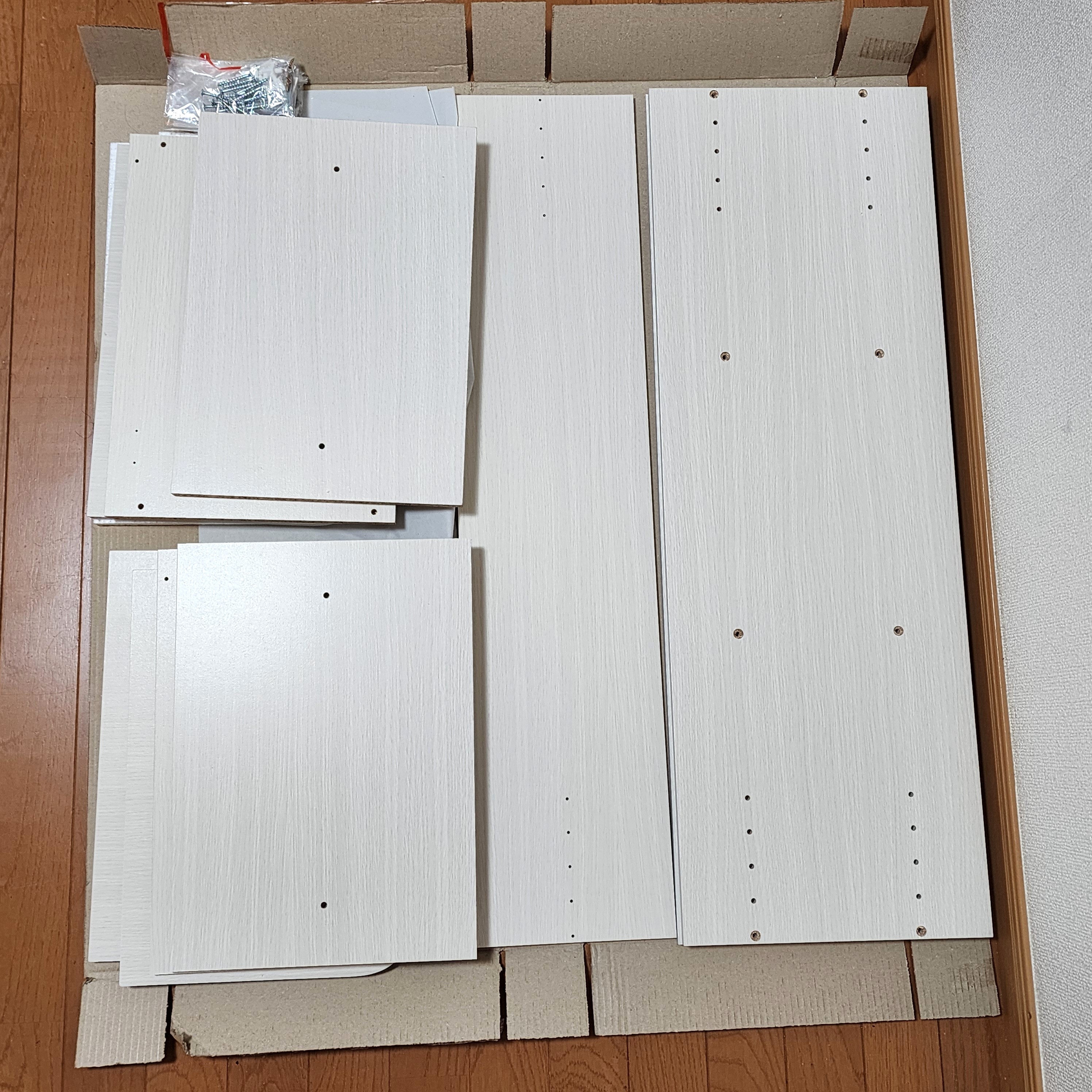 穴の開いた板材とネジが段ボールに収まっている。組み立て用の家具キットの一部。