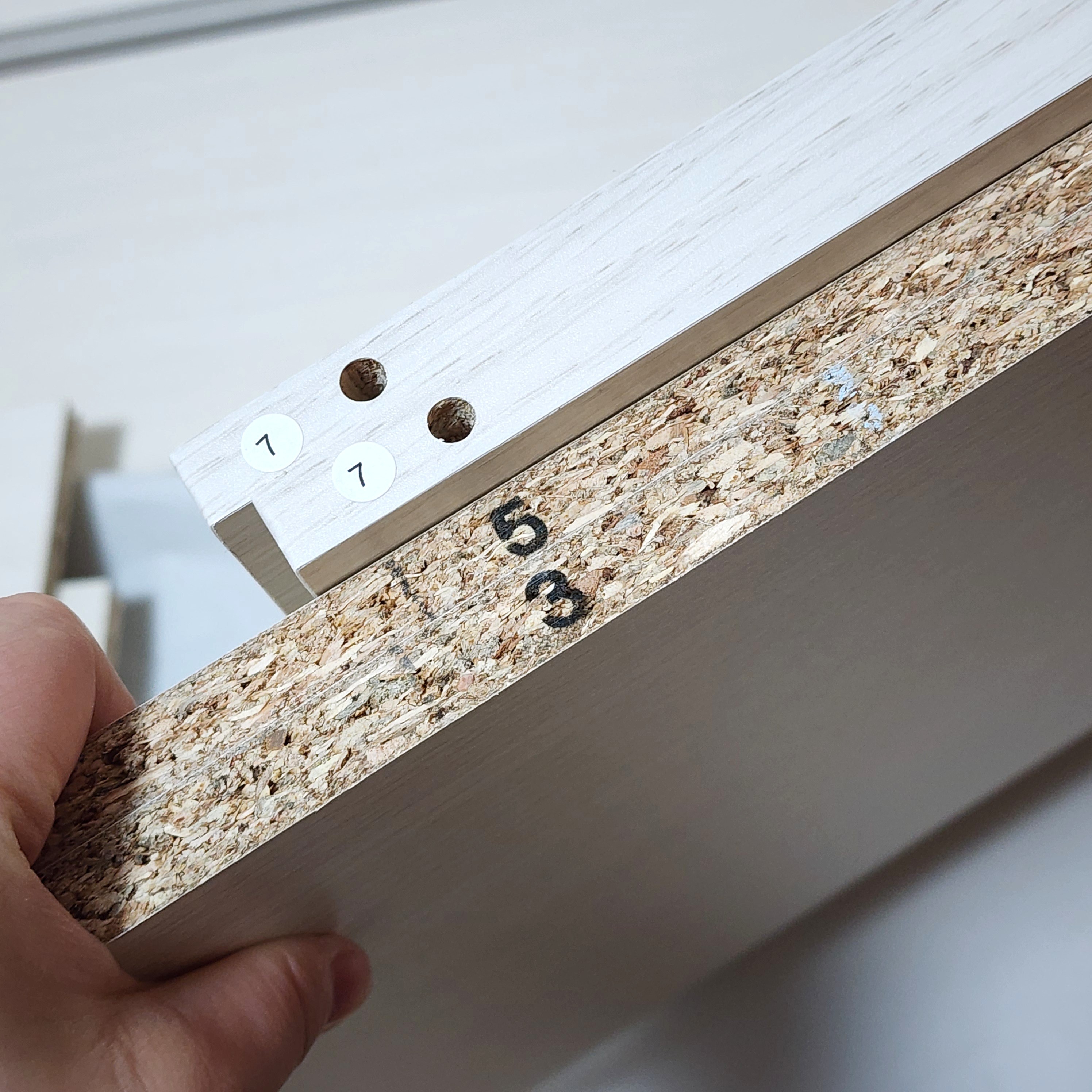 組み立て中の家具用に2つの木製パネルが角度を付けて接合されています。手が片方のパネルを支えています。