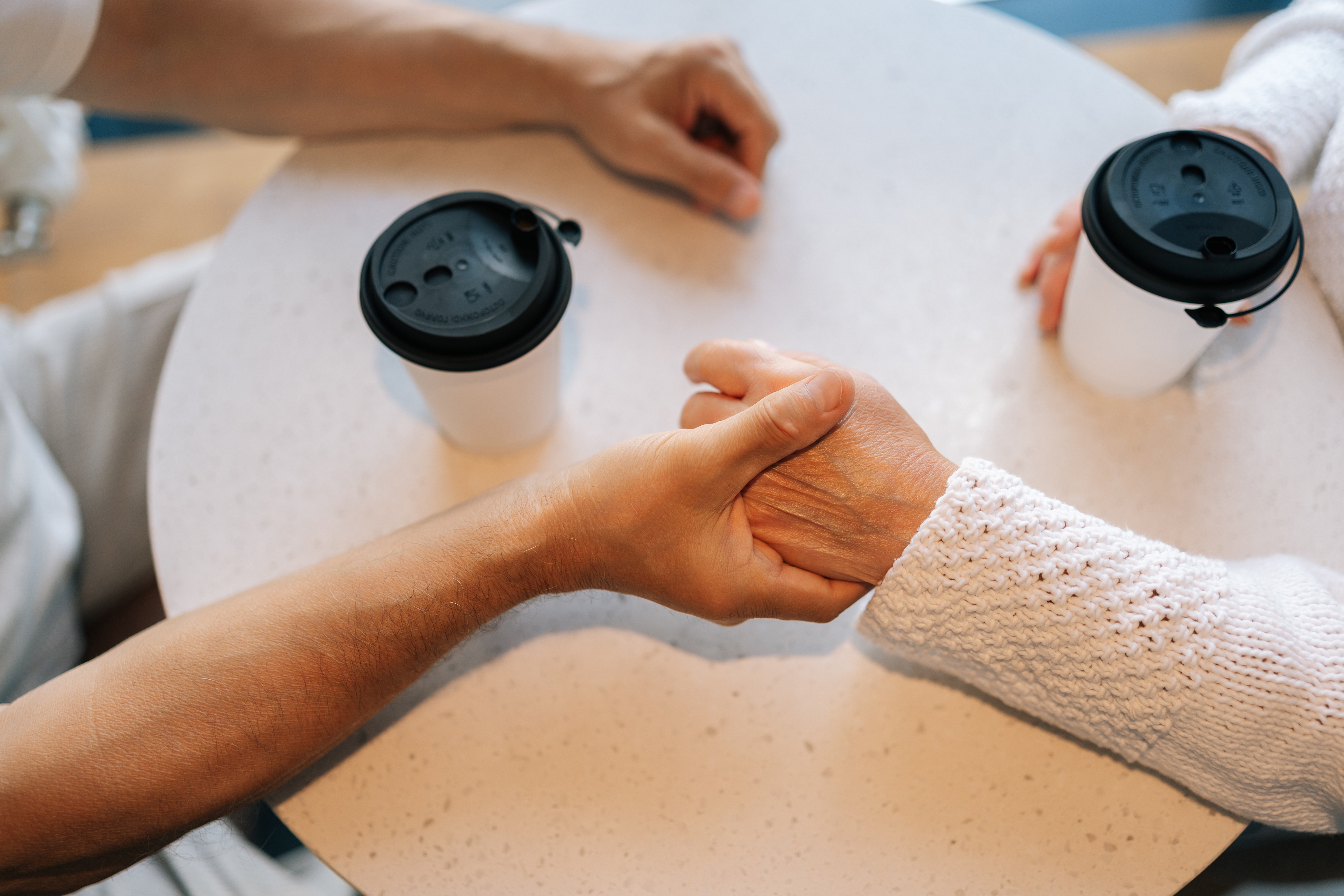 Two people holding hands across a table with coffee cups, symbolizing connection and companionship