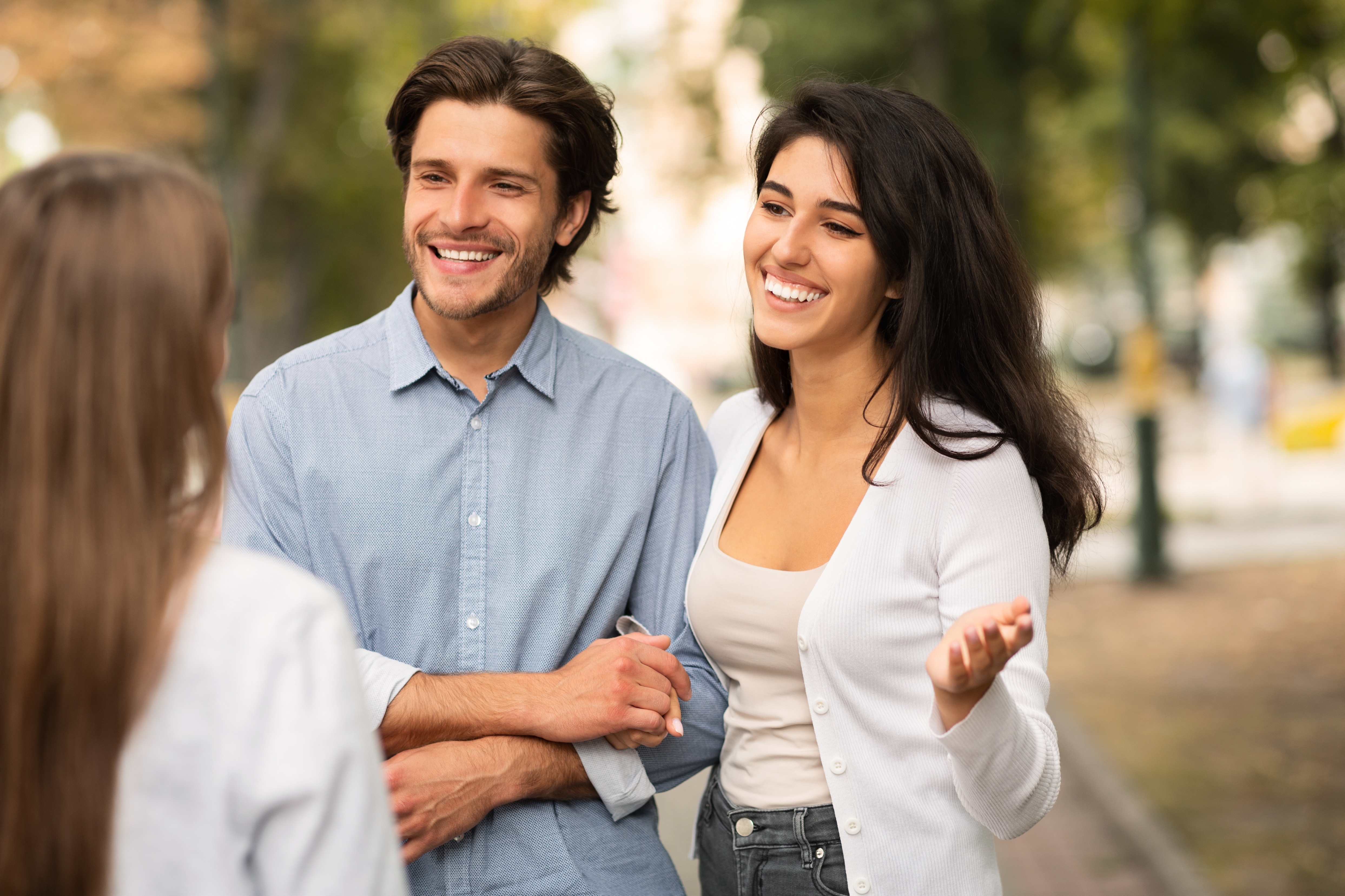 Three people are outdoors having a friendly conversation. A man and a woman are smiling and looking at a third person in the foreground