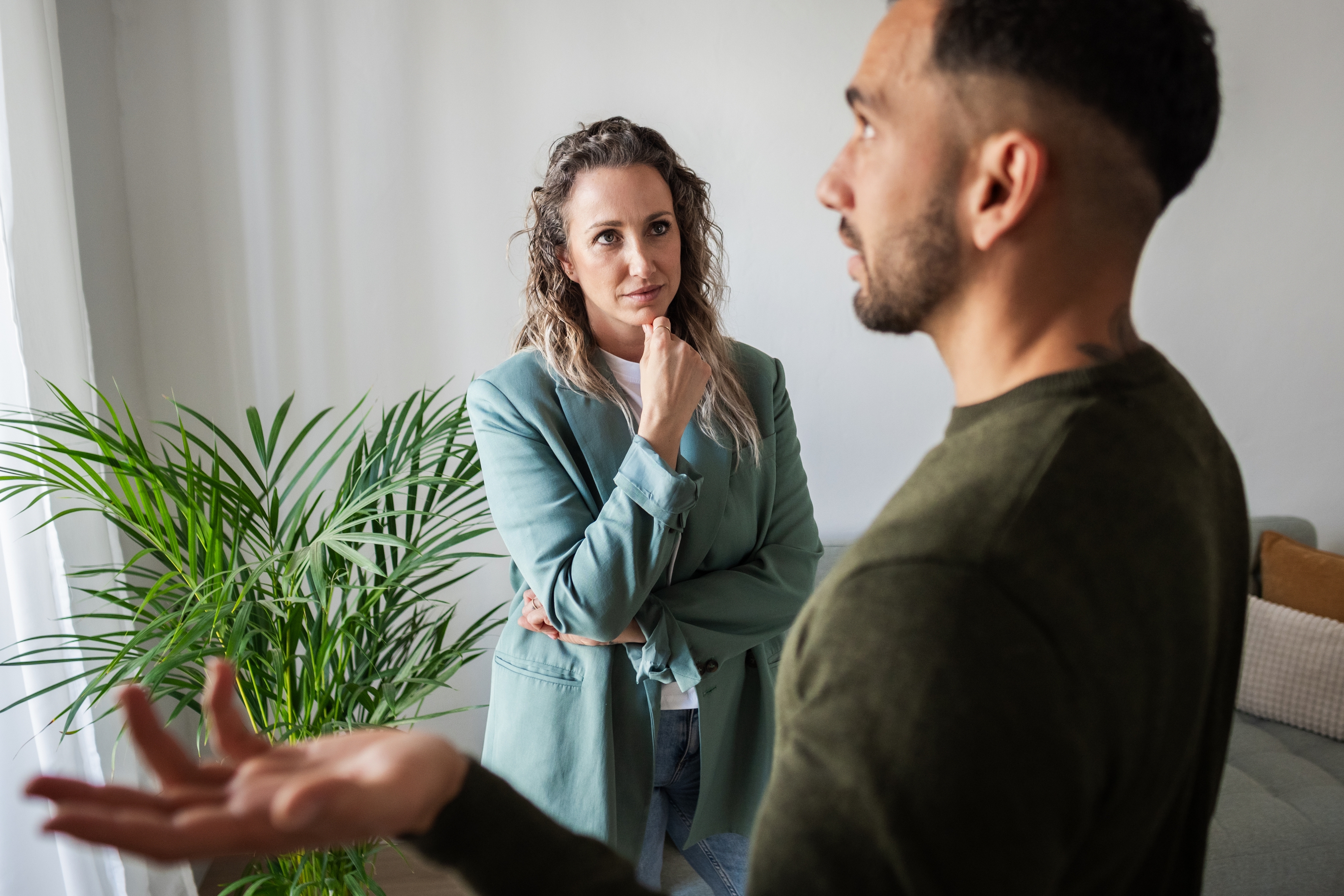 Two people having a conversation indoors; a woman in a blazer listens attentively to a man speaking animatedly