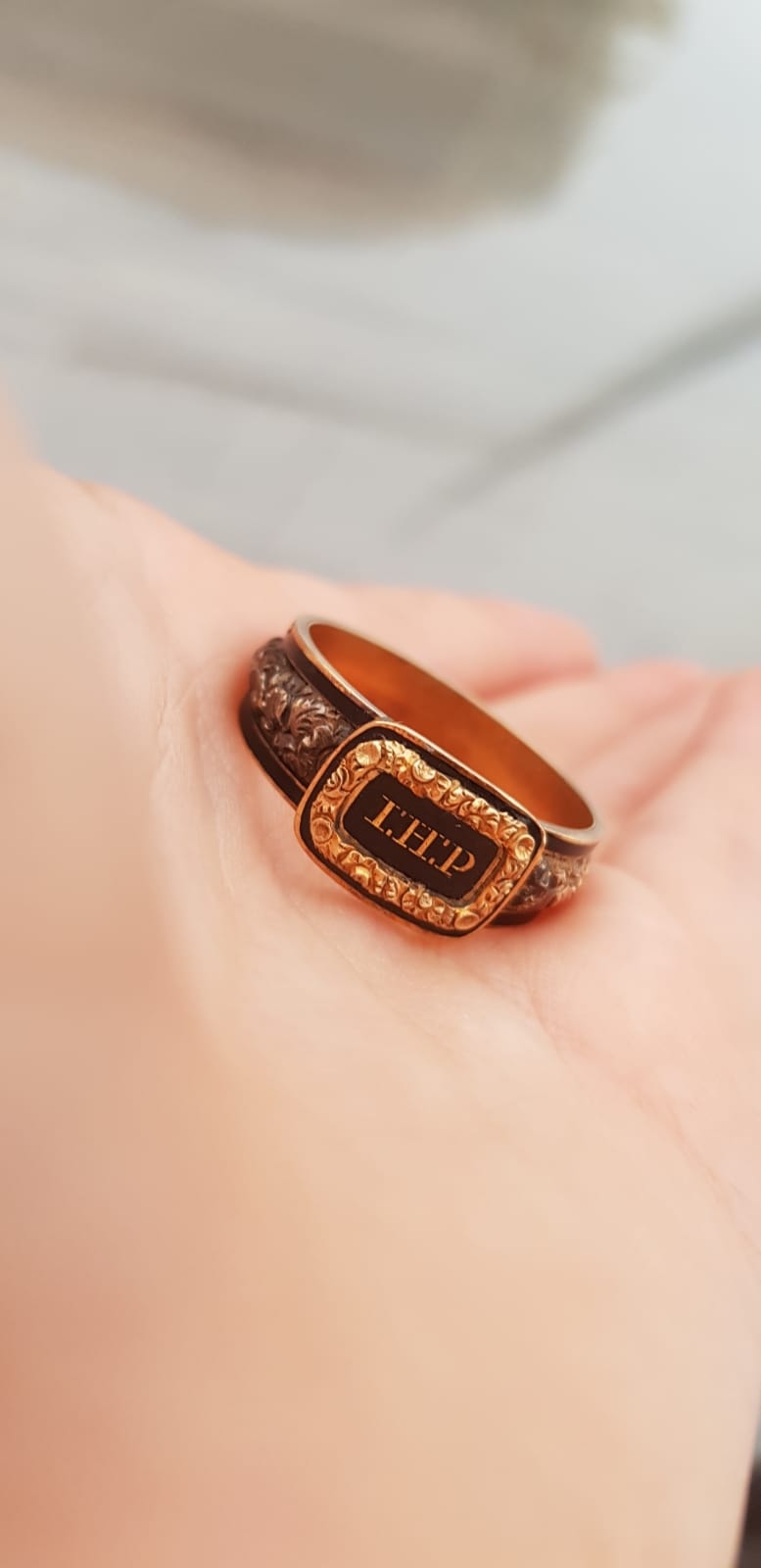 A close-up of a hand holding a bronze ring with an engraved plate that reads "T.H.P."