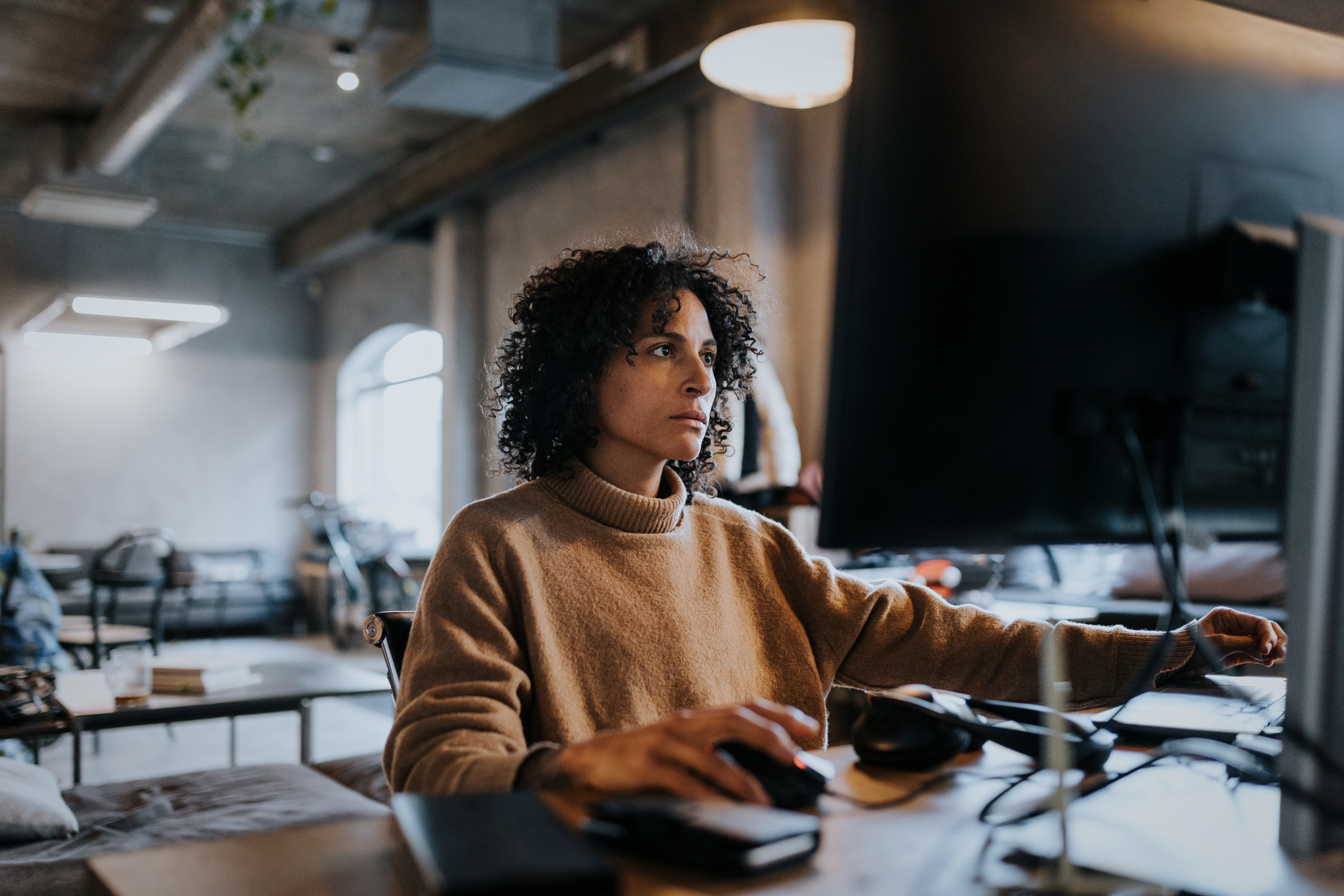 Person in a cozy sweater intensely focused on a large computer monitor in a stylish, modern workspace