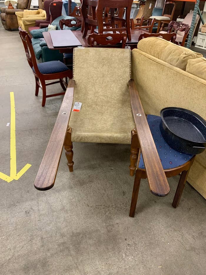 Unique chair with extended wooden armrests on a furniture showroom floor, surrounded by other used furniture pieces