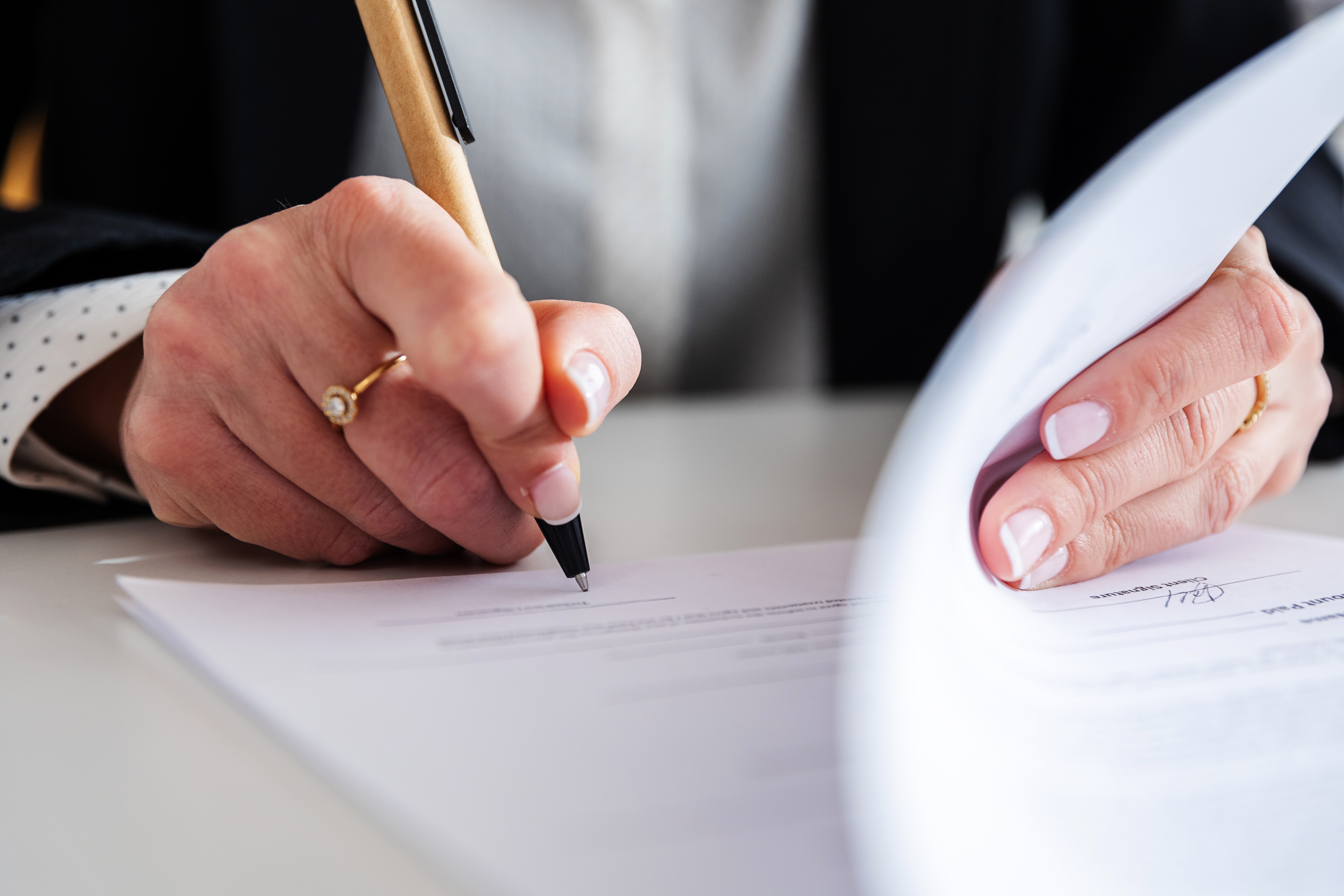 Person signing a document with a pen, focusing on their hands