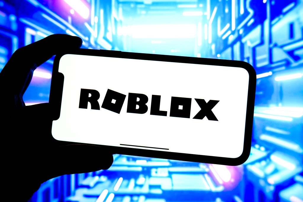 Person holding phone with "Roblox" on screen, against a futuristic, digital-themed background