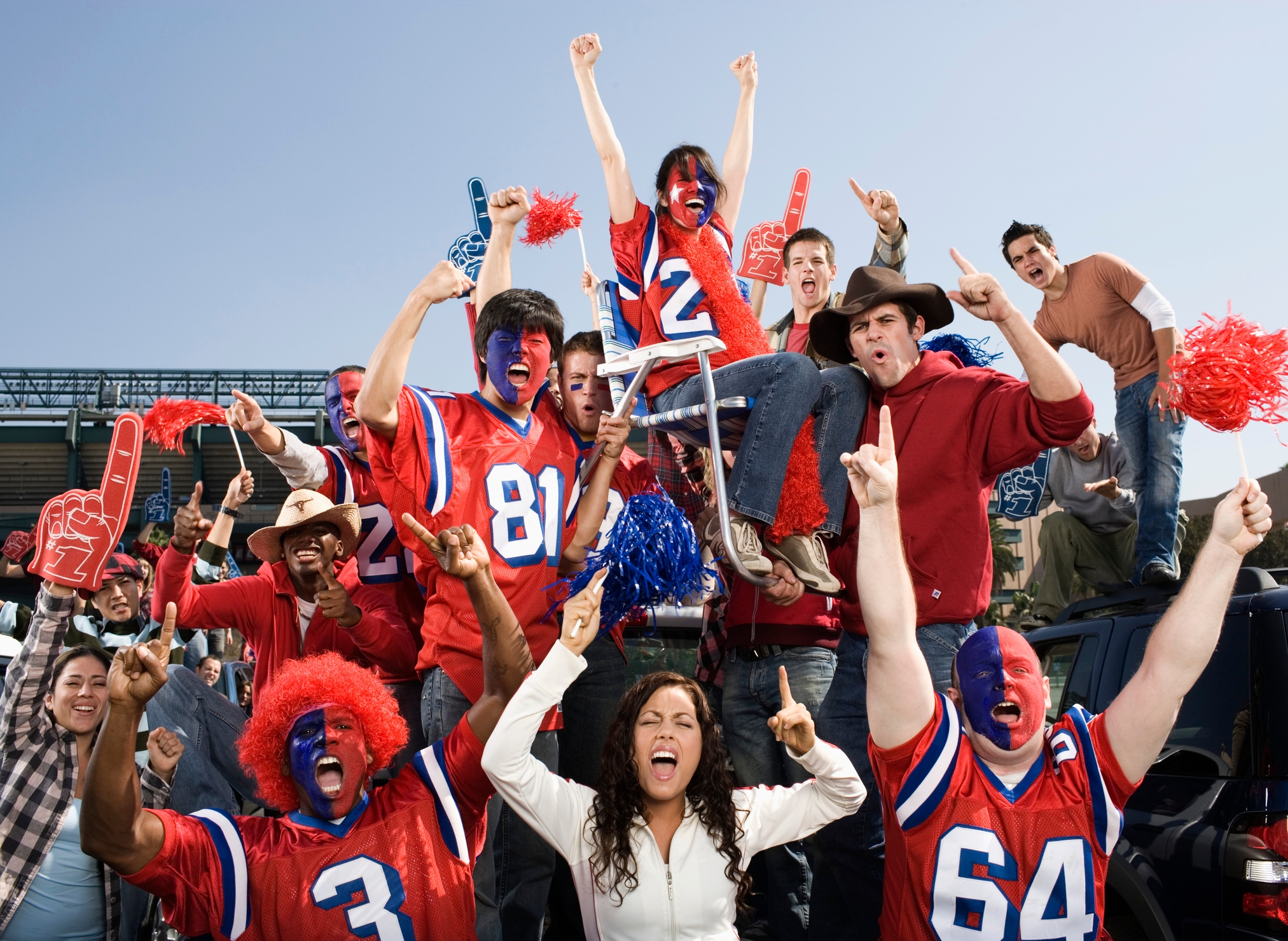 Group of excited sports fans in team jerseys and face paint cheering, with one fan in a wheelchair
