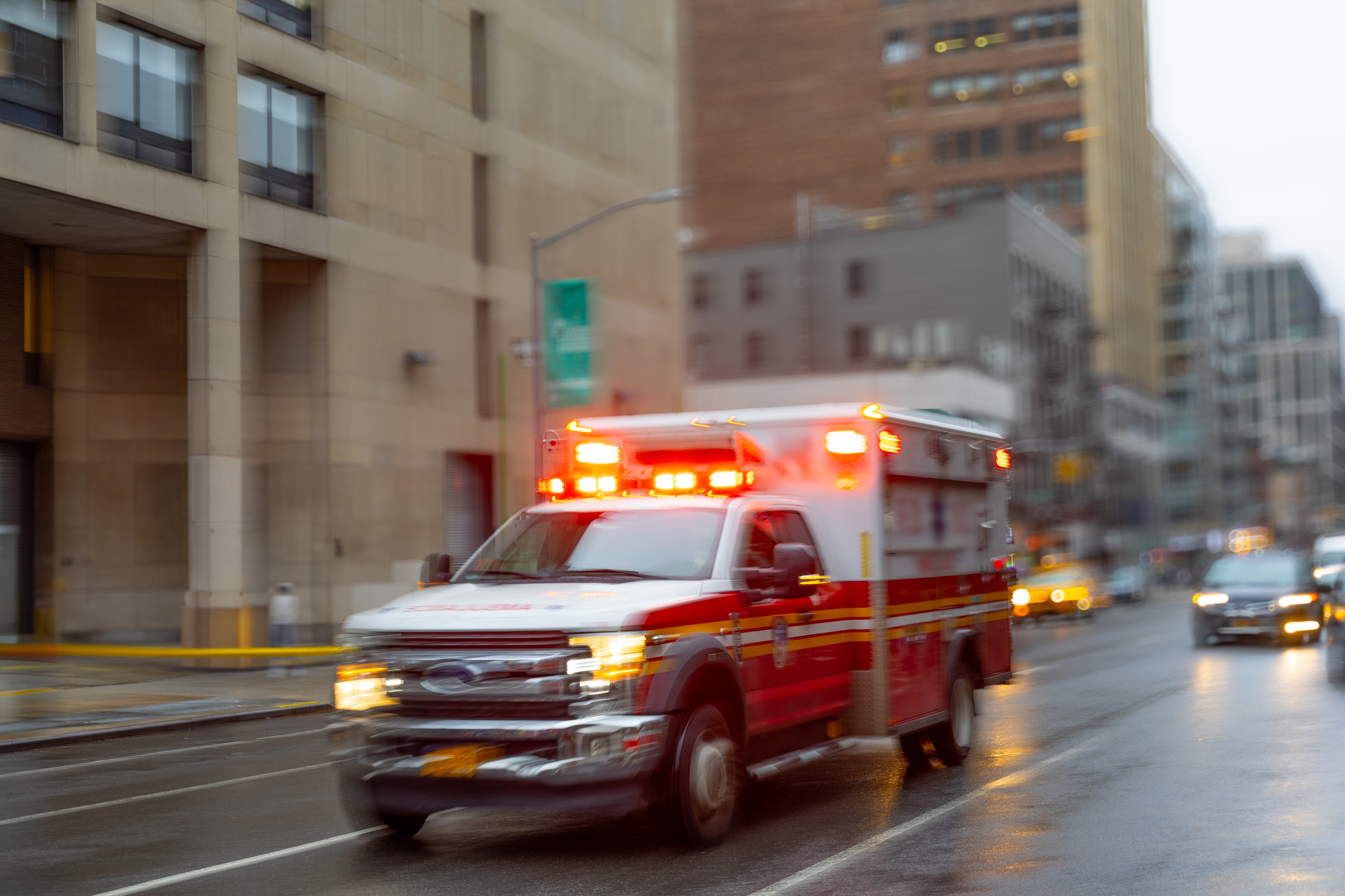 Ambulance with flashing lights driving on a city street with blurred buildings in the background