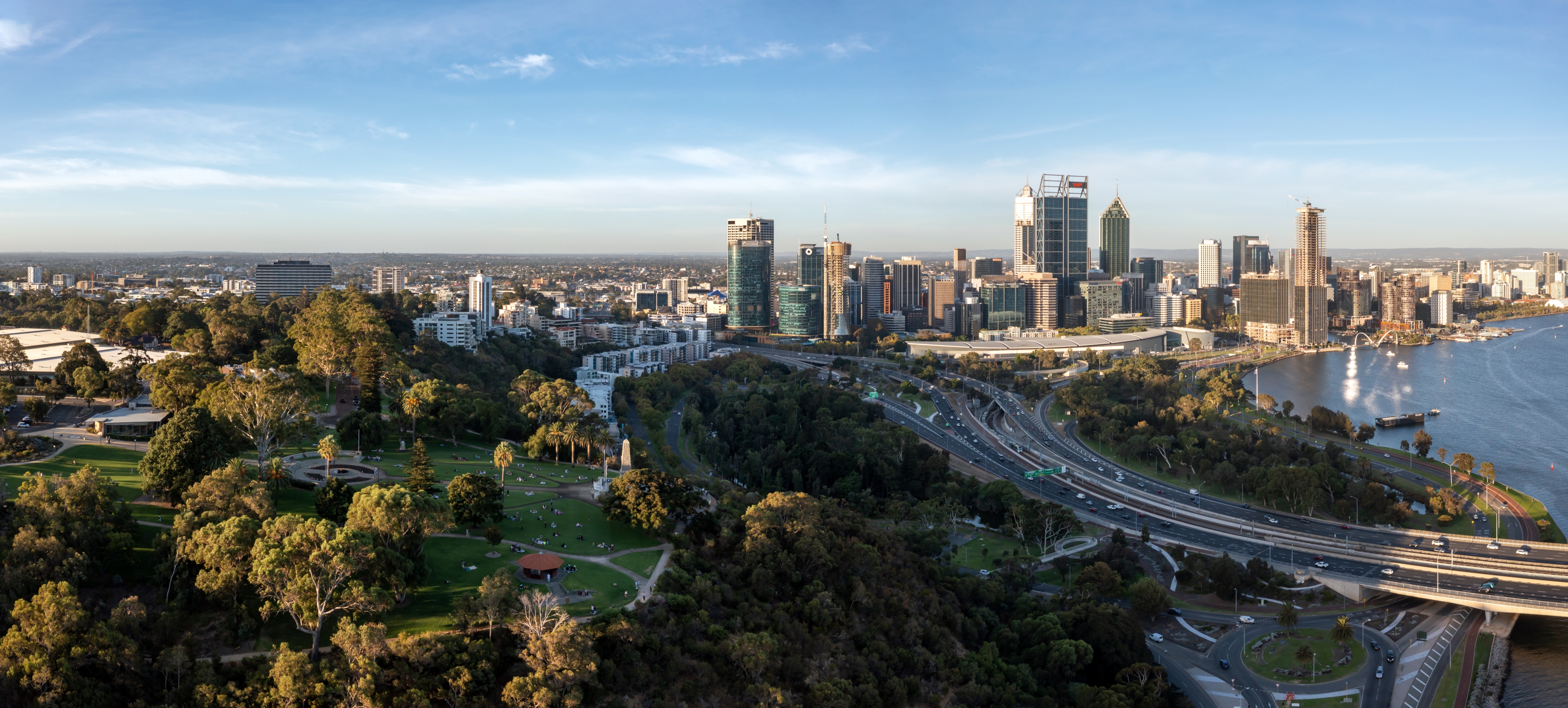 Aerial view of a city skyline with tall buildings, a river, and a surrounding park area with trees and pathways