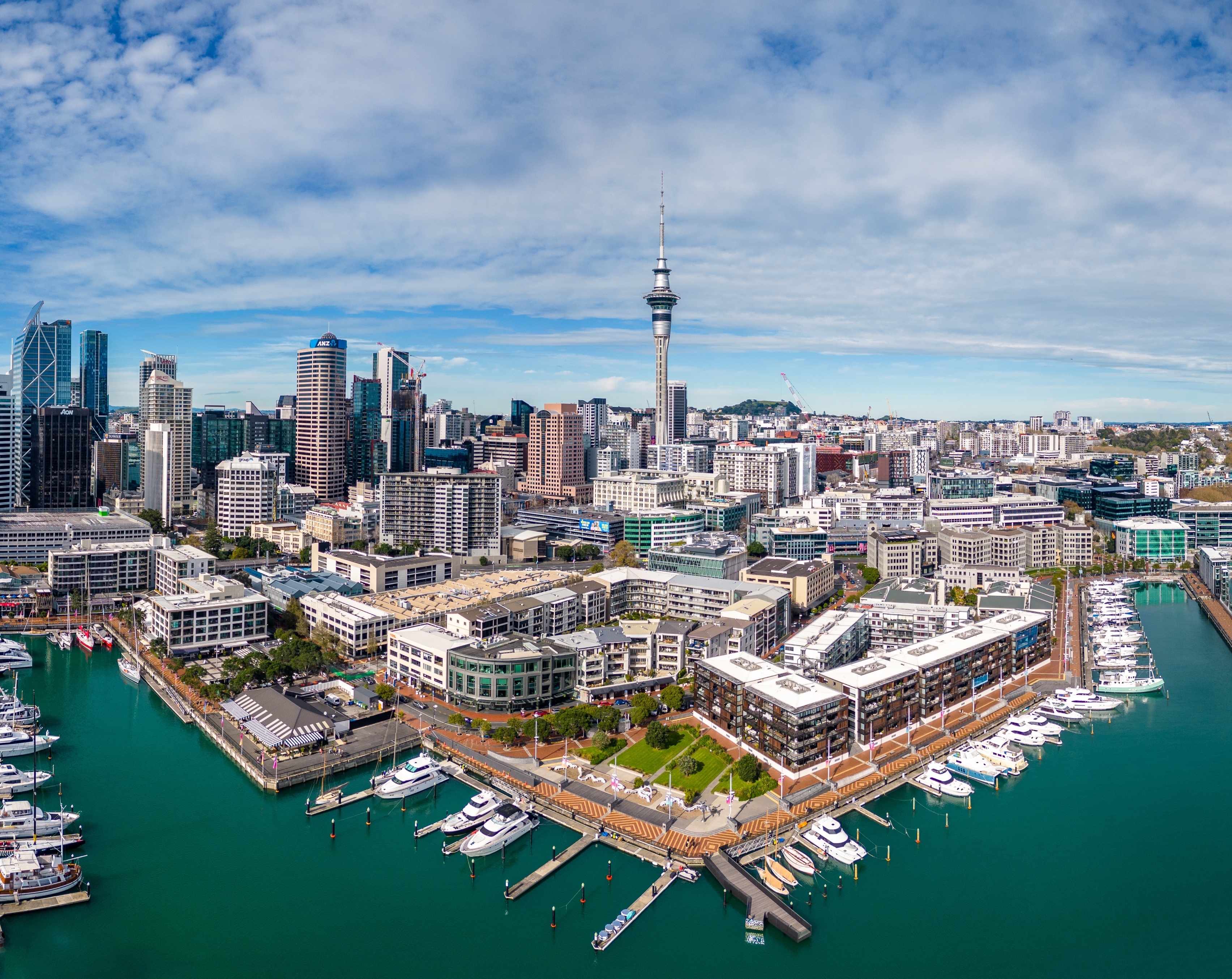 Aerial view of a bustling city skyline and marina with numerous boats, dominated by a tall central tower
